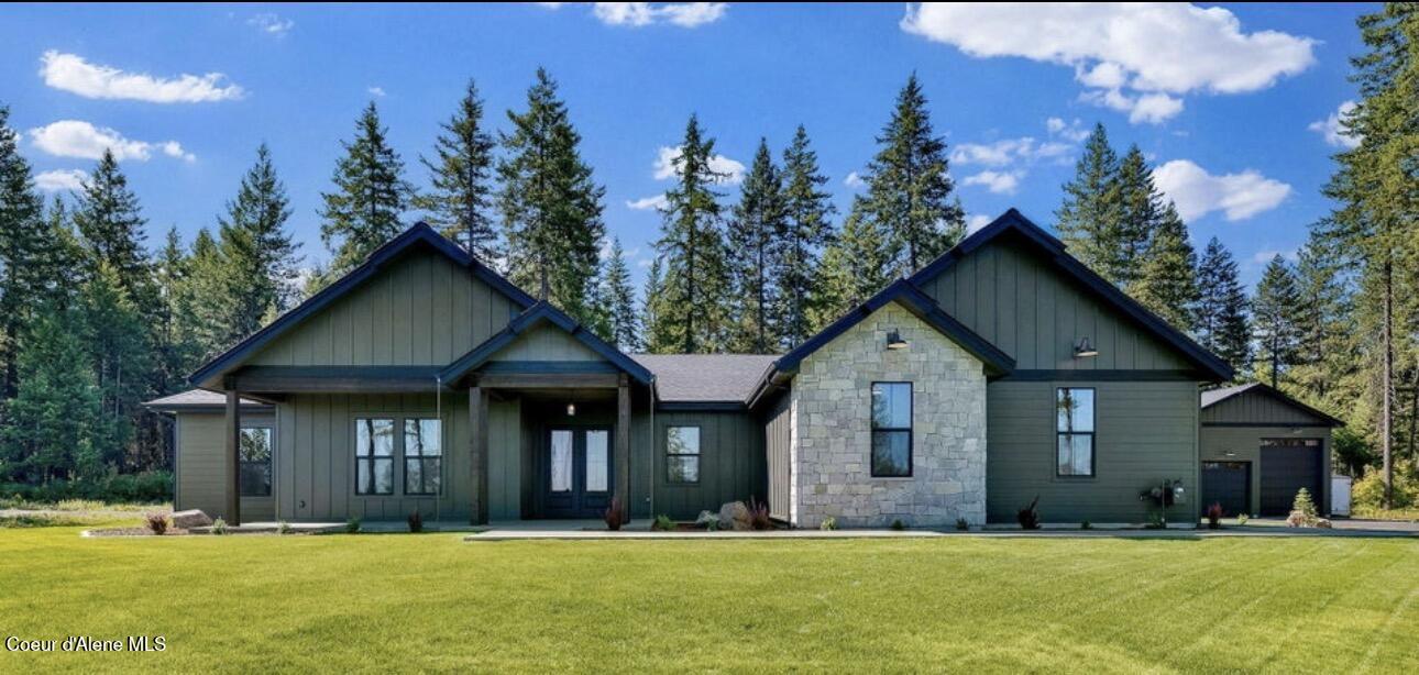 Single-story green home with a stone facade, attached garage, and broad lawn backed by evergreens.