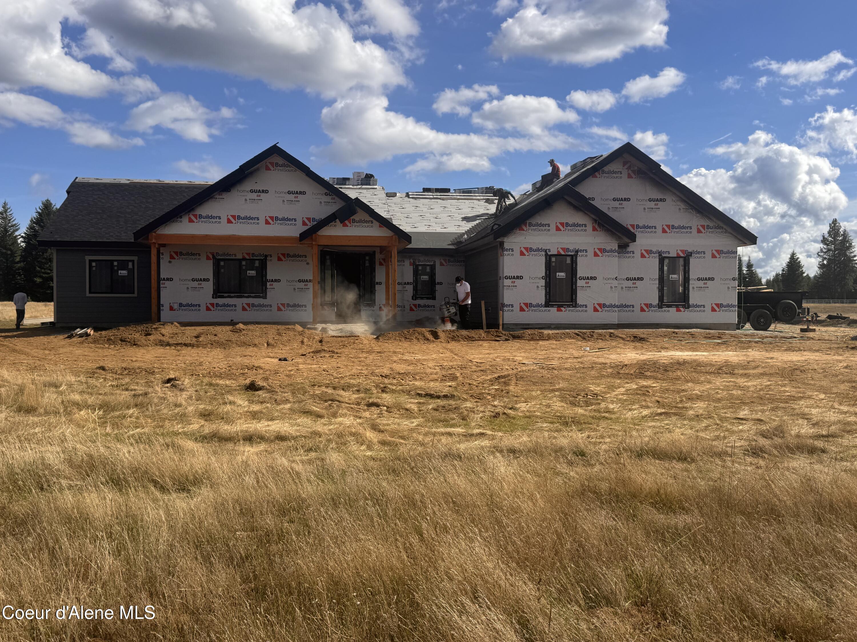 House under construction on a dry grassy lot, with workers on the roof and at the entrance.