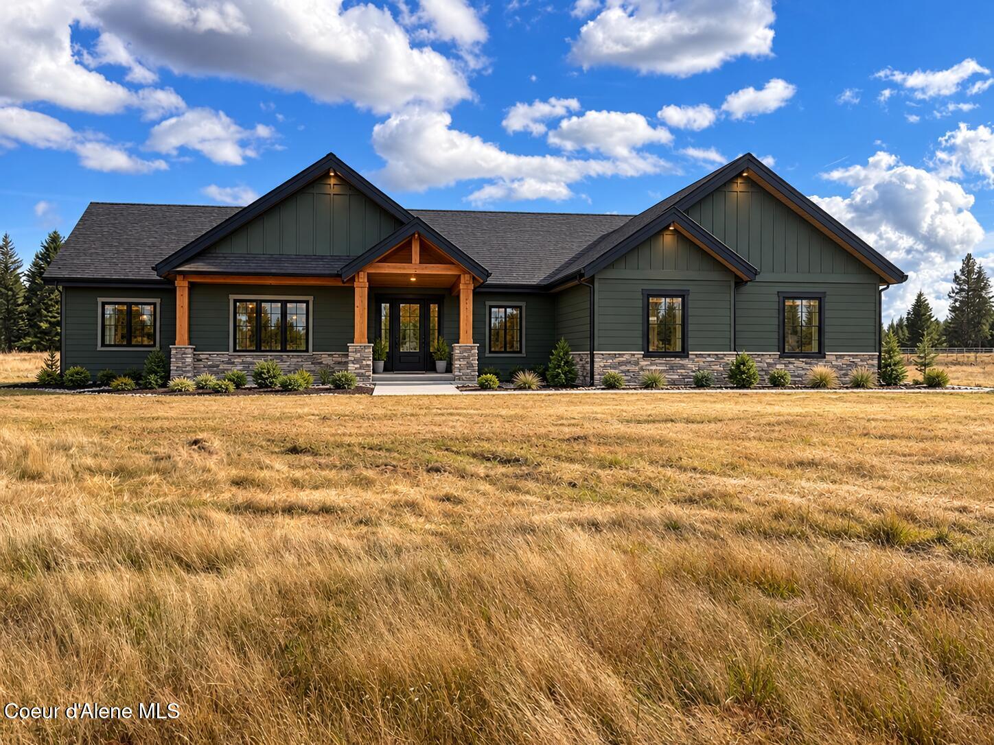 Green single-story home with stone accents and a timber-covered entry, set behind a golden-grass field.