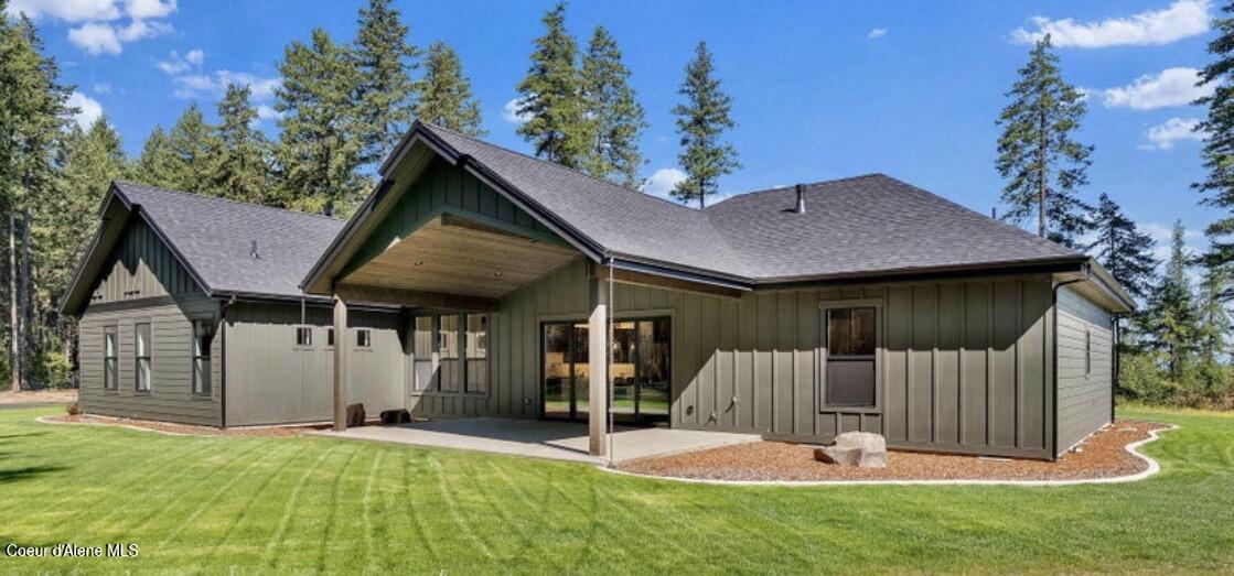 Rear exterior of a dark green home with a covered patio and lawn, surrounded by evergreen trees.