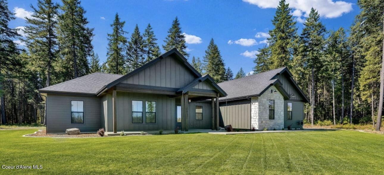 Modern gray single-story home with stone accents, a broad lawn, and evergreen trees.