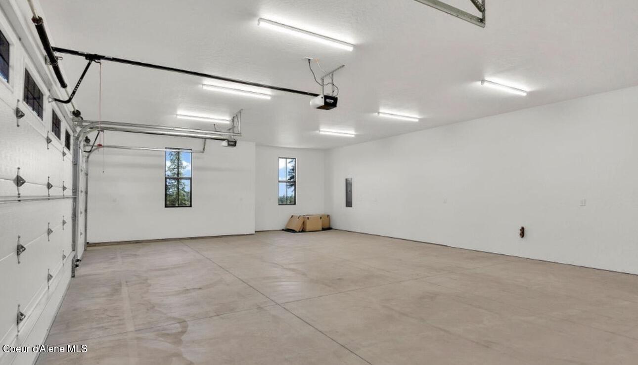 Spacious empty garage with a concrete floor, overhead door, fluorescent lights, and two narrow windows.