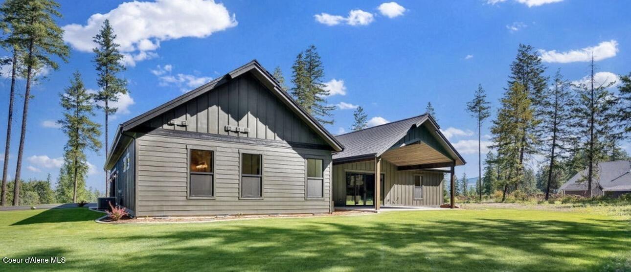 Gray-sided home with a covered patio, broad lawn, and tall pine trees.