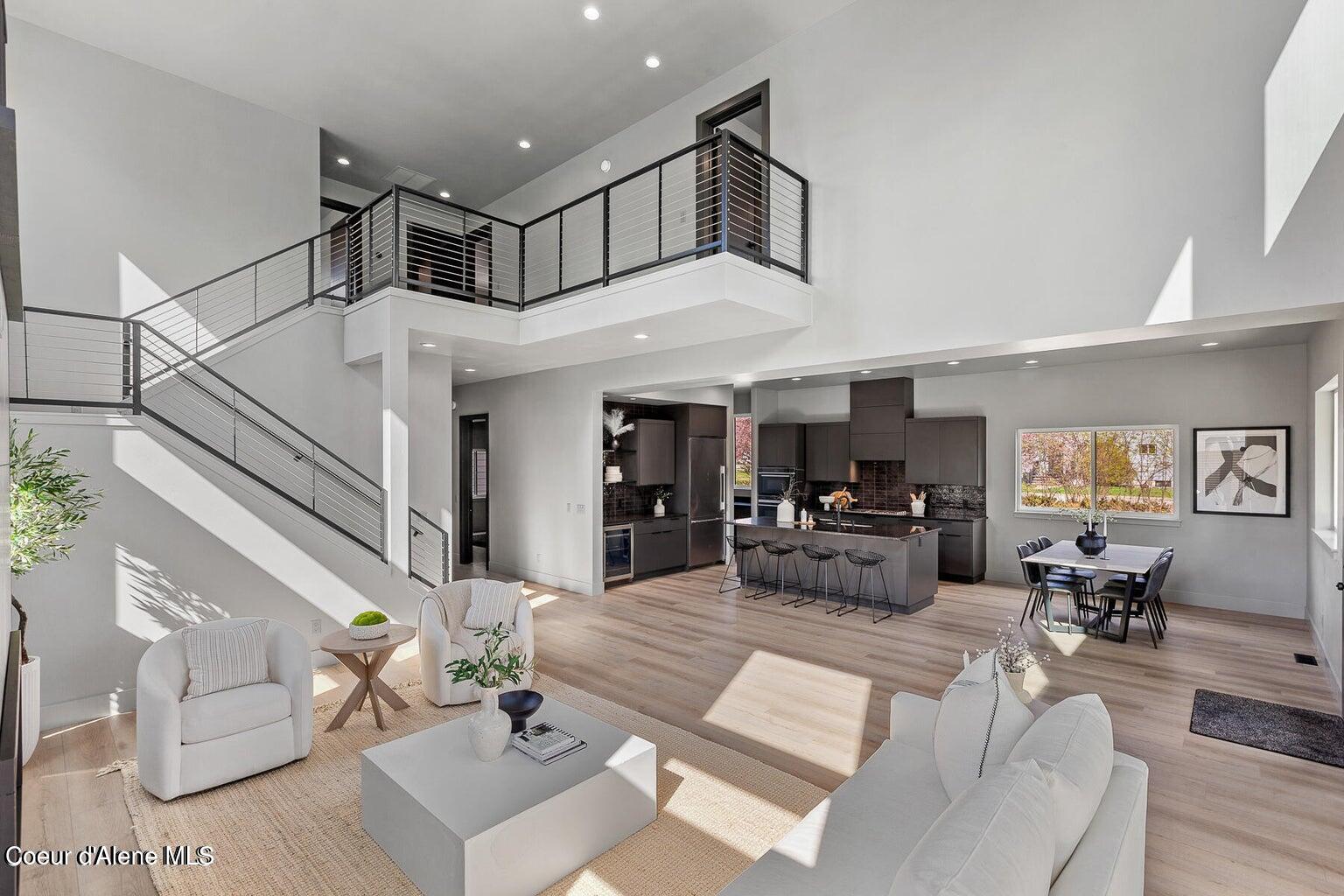 Open-concept living area with a soaring ceiling, modern kitchen, and staircase to an upper-level landing.
