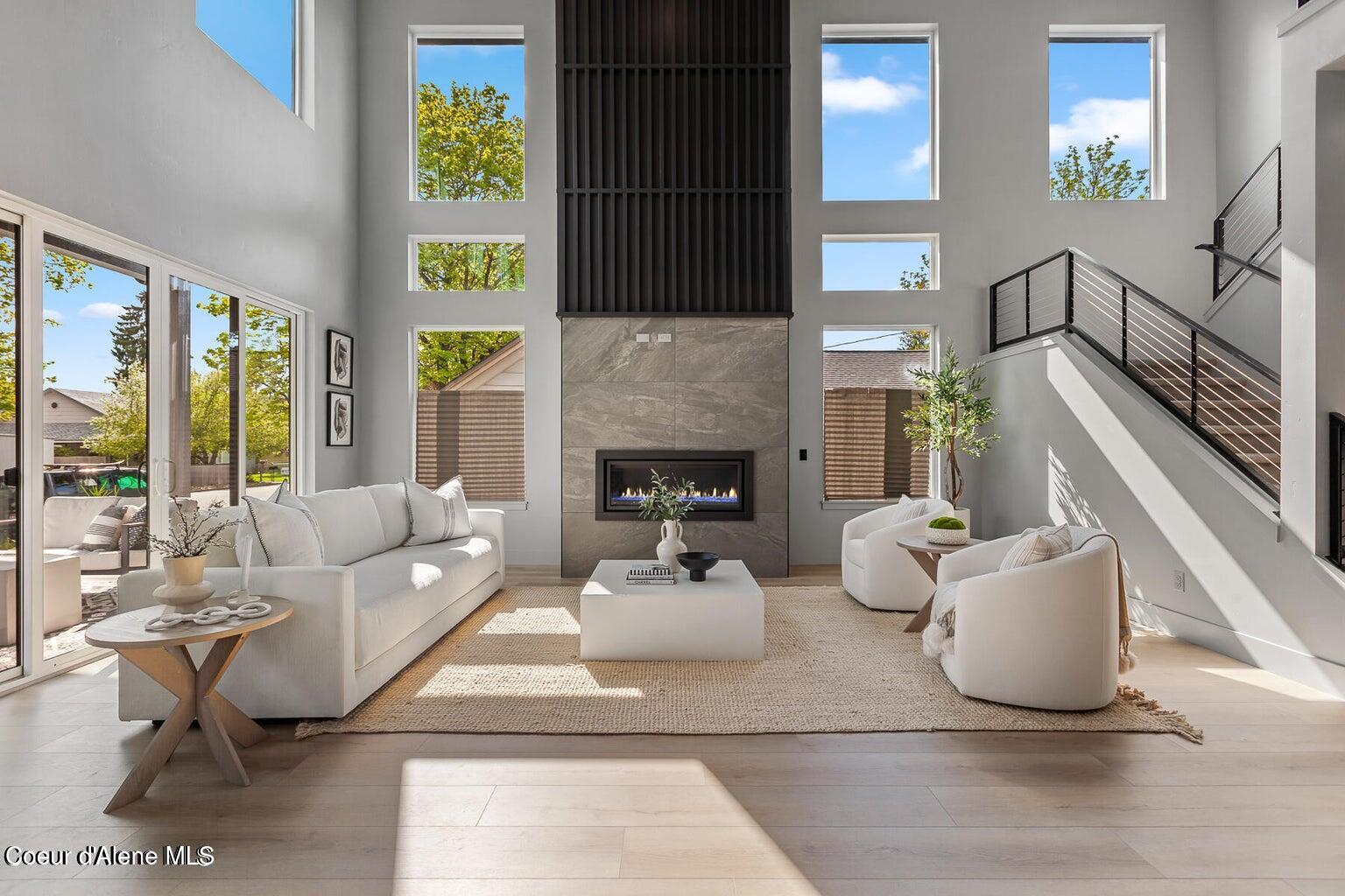 Two-story living room with a tall tiled fireplace, large windows, white seating, and an open staircase.