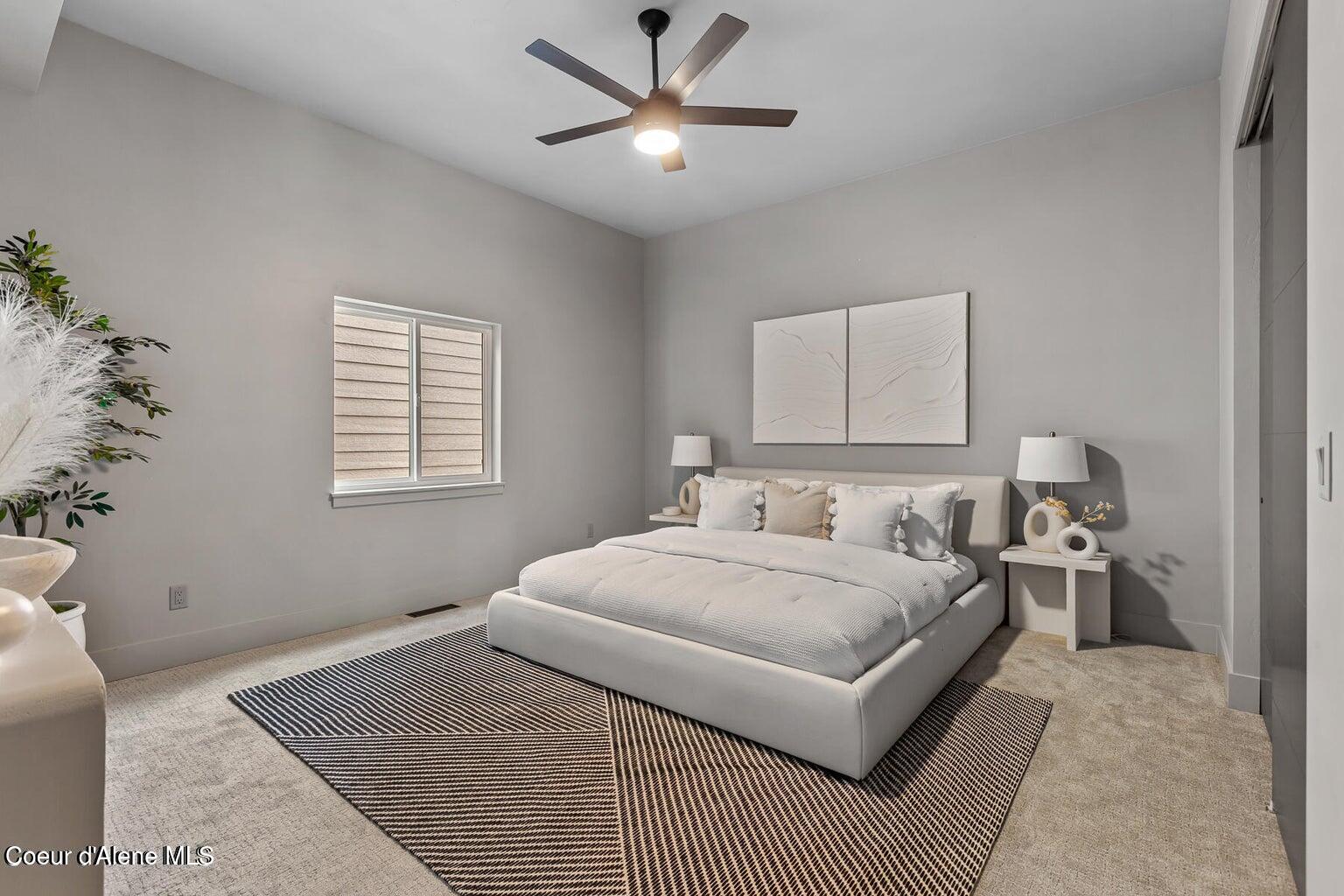 Staged bedroom with a white upholstered bed, geometric rug, ceiling fan, and abstract wall art.