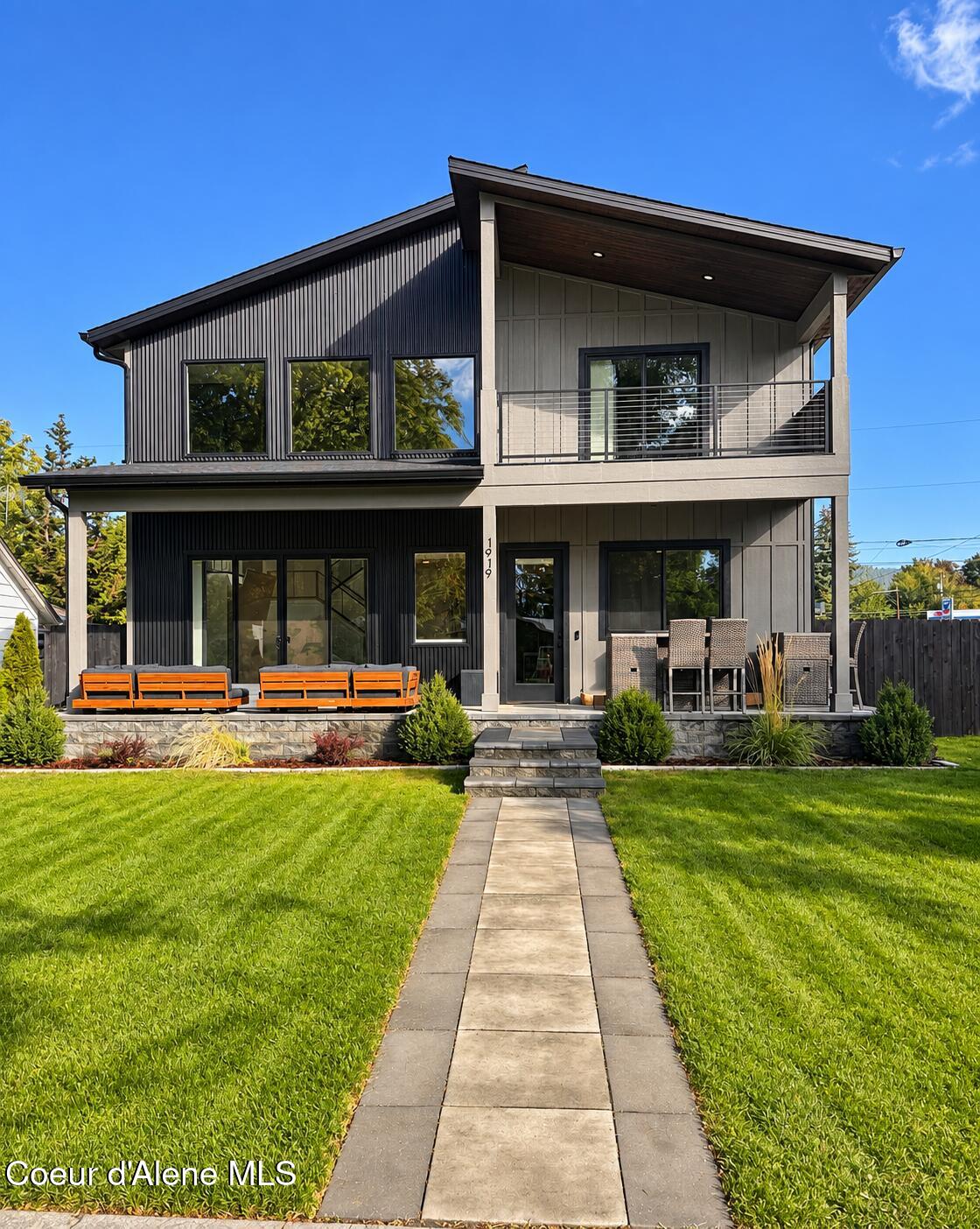 Modern two-story gray home with a covered balcony, stone patio, and walkway through the lawn.