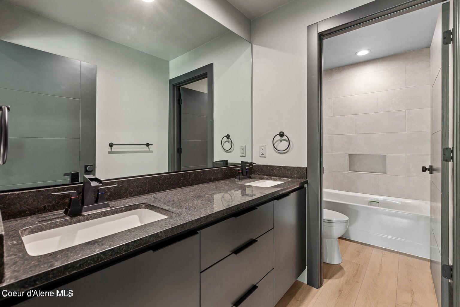 Bathroom with a dark double-sink vanity, large mirror, and tiled tub surround.