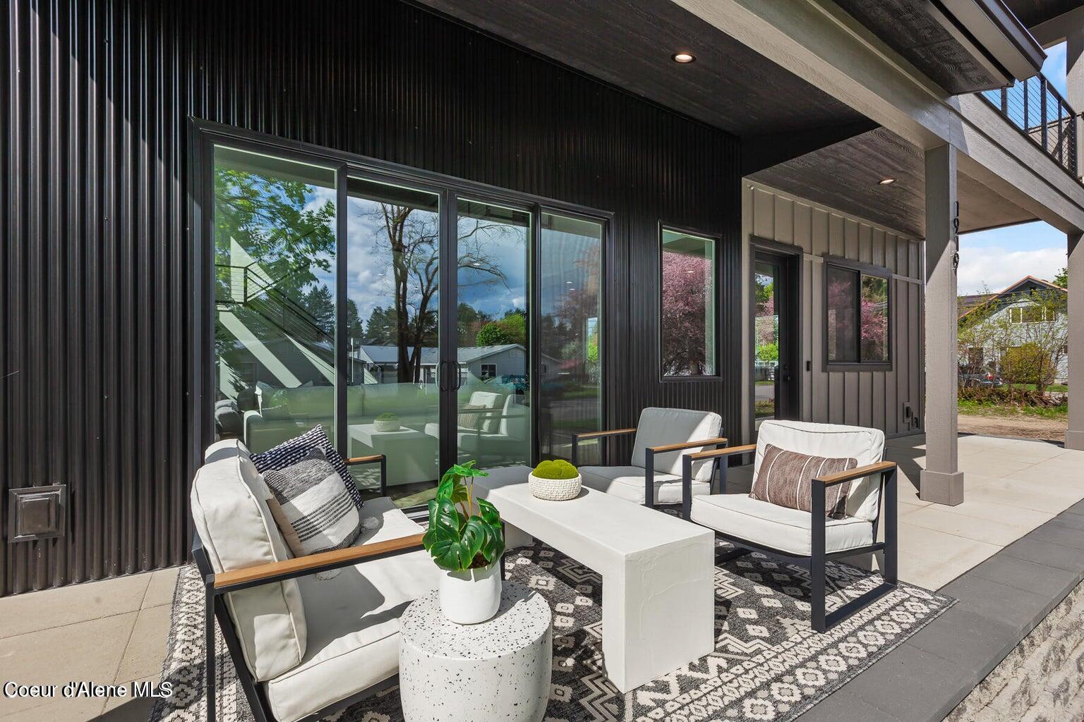 Covered patio with white lounge seating and a patterned rug beside black siding and sliding glass doors.