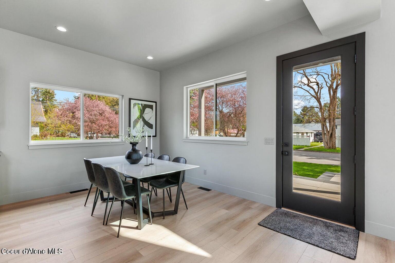 Dining area with a white table, pale wood floors, and a black-framed glass front door.