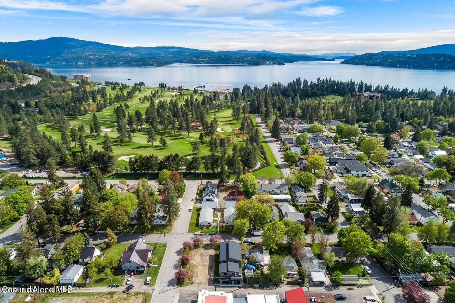Aerial panorama of a Coeur d'Alene neighborhood, golf course, lake, and wooded mountains.