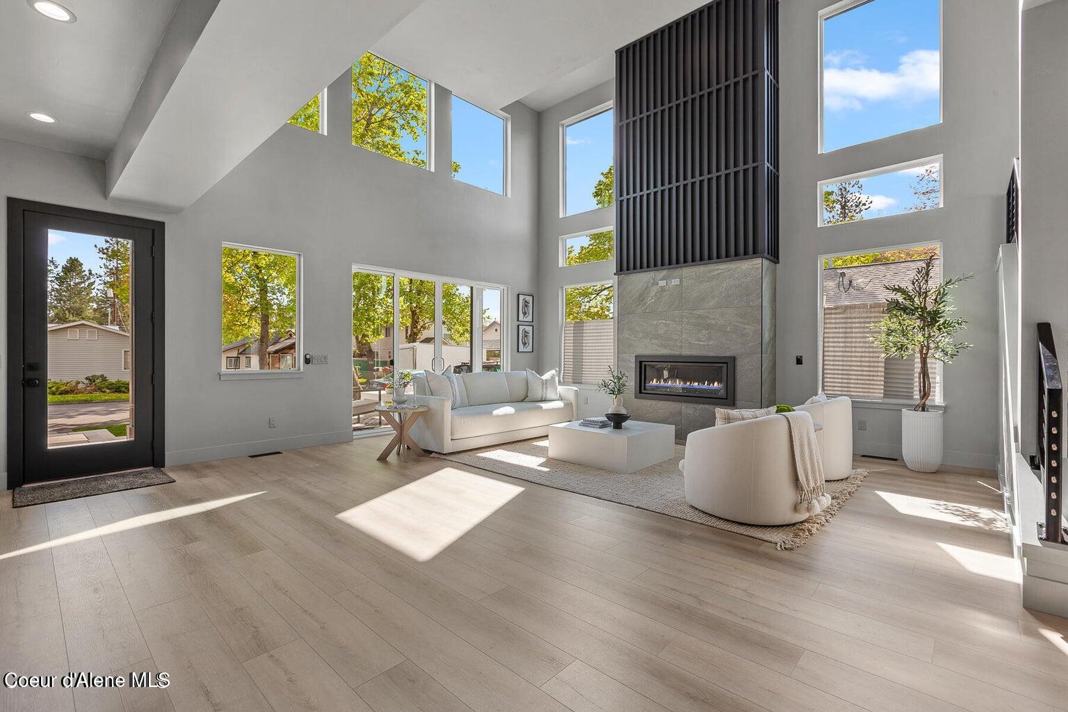 Double-height living room with tall windows, a stone fireplace, and white sofas.