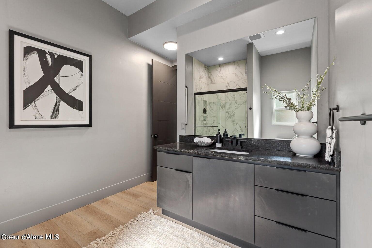 Modern bathroom vanity with dark stone countertop and a marble-look tiled glass shower.