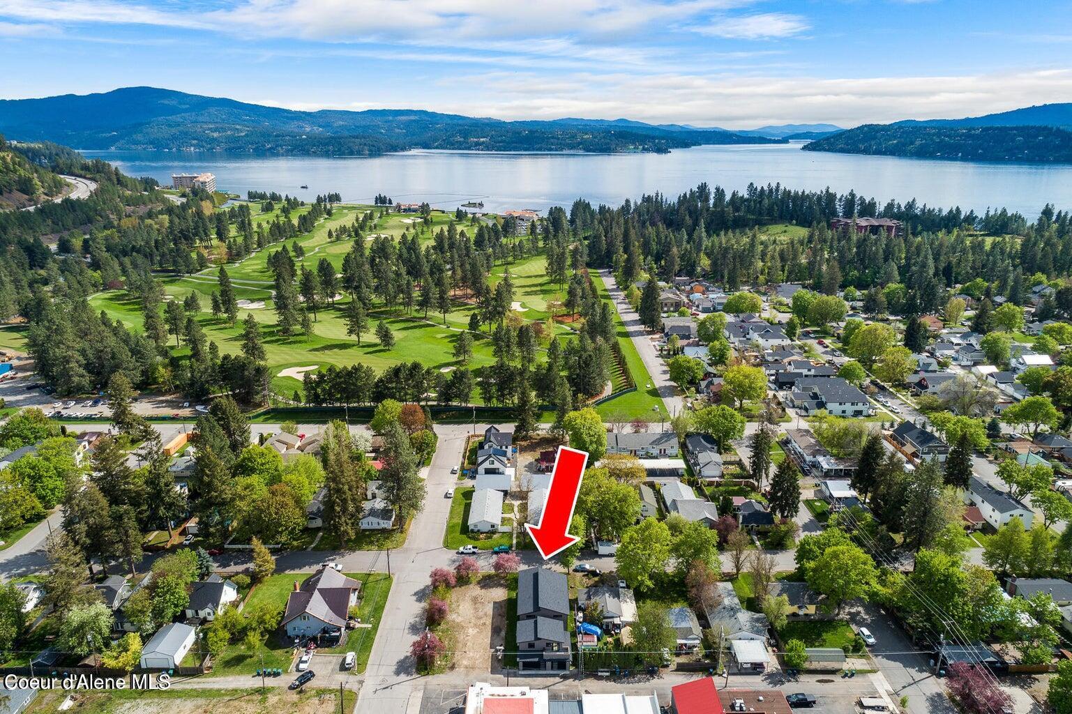 Aerial view of a Coeur d'Alene property marked by a red arrow, with a golf course and lake beyond.