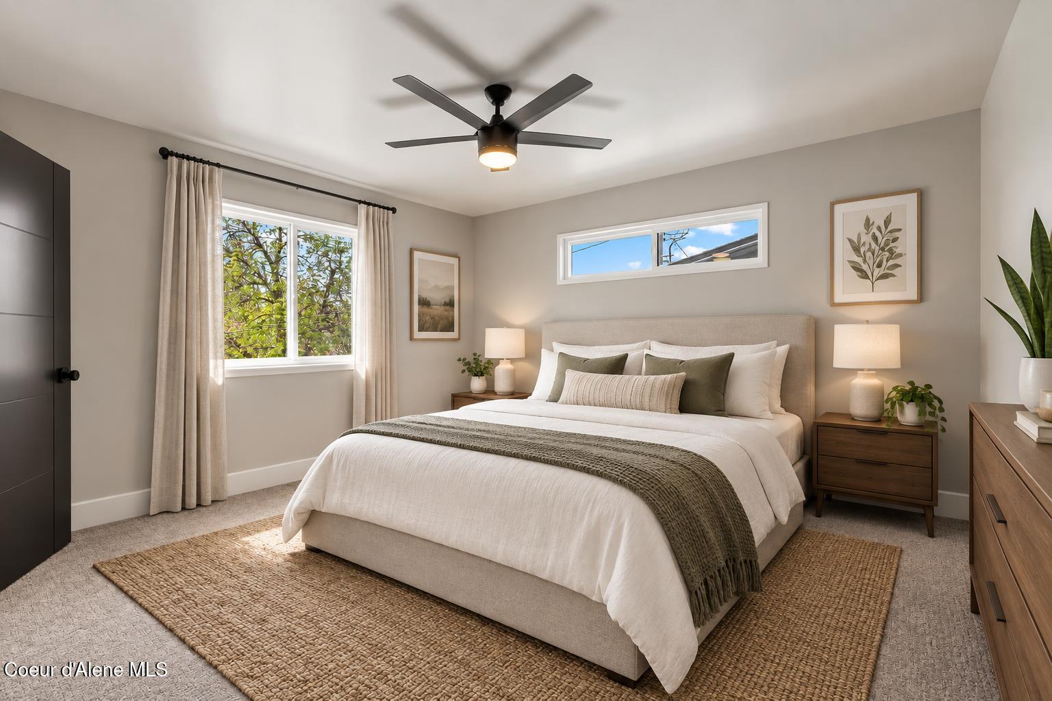 Staged bedroom with an upholstered bed, olive throw, ceiling fan, and large windows.