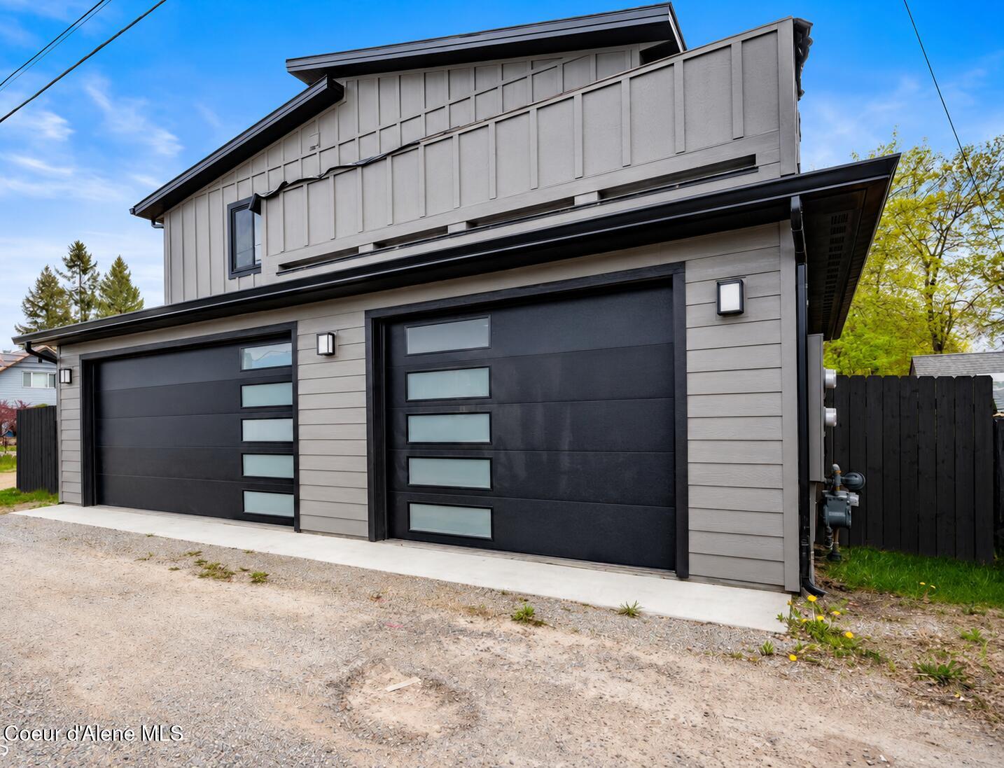 Modern two-story home with light gray siding and two black garage doors with frosted windows.