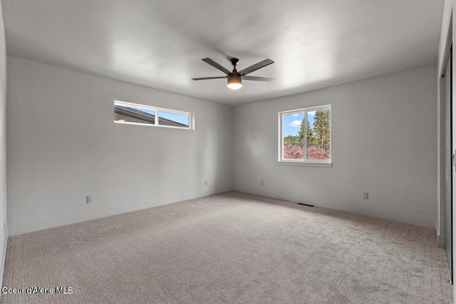 Vacant carpeted bedroom with a ceiling fan and windows overlooking flowering trees.