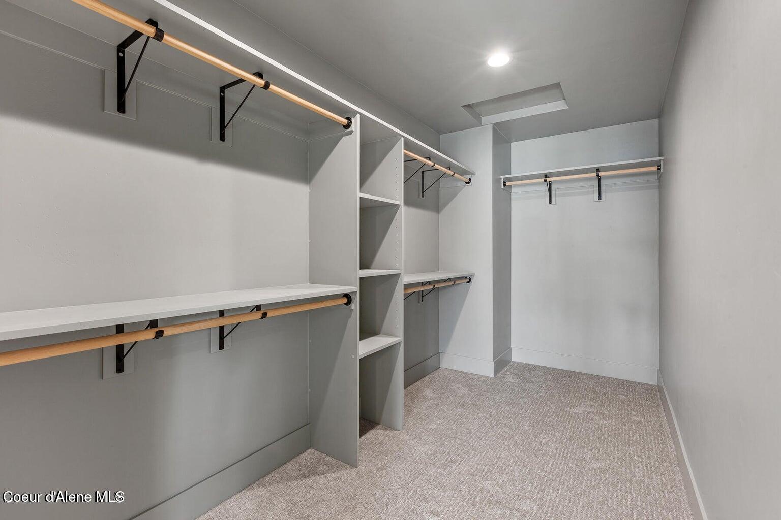Walk-in closet with built-in shelving, wooden hanging rods, and beige carpet.