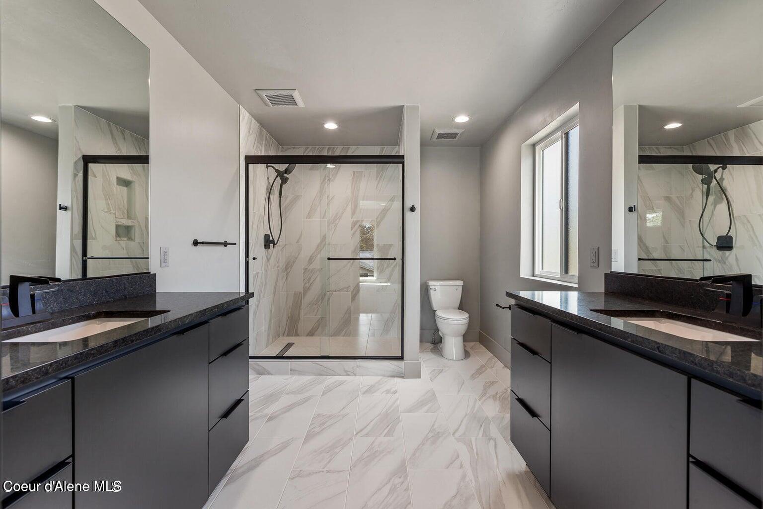 Modern bathroom with a marble-look walk-in shower and dark double vanities.