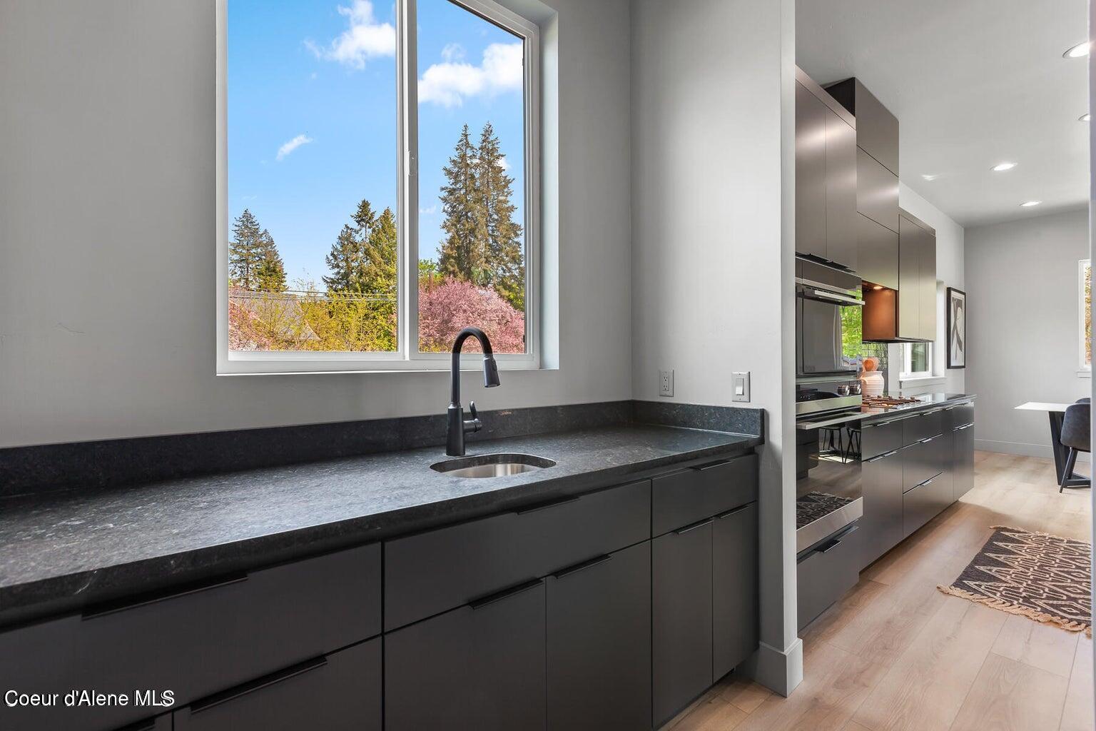Modern kitchen with dark cabinetry, stone counters, and a large window overlooking spring trees.