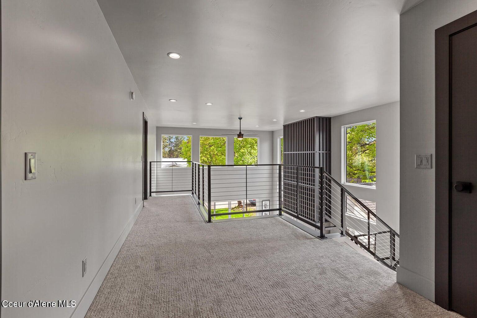 Upstairs landing with gray carpet, black metal stair railings, and windows overlooking trees.