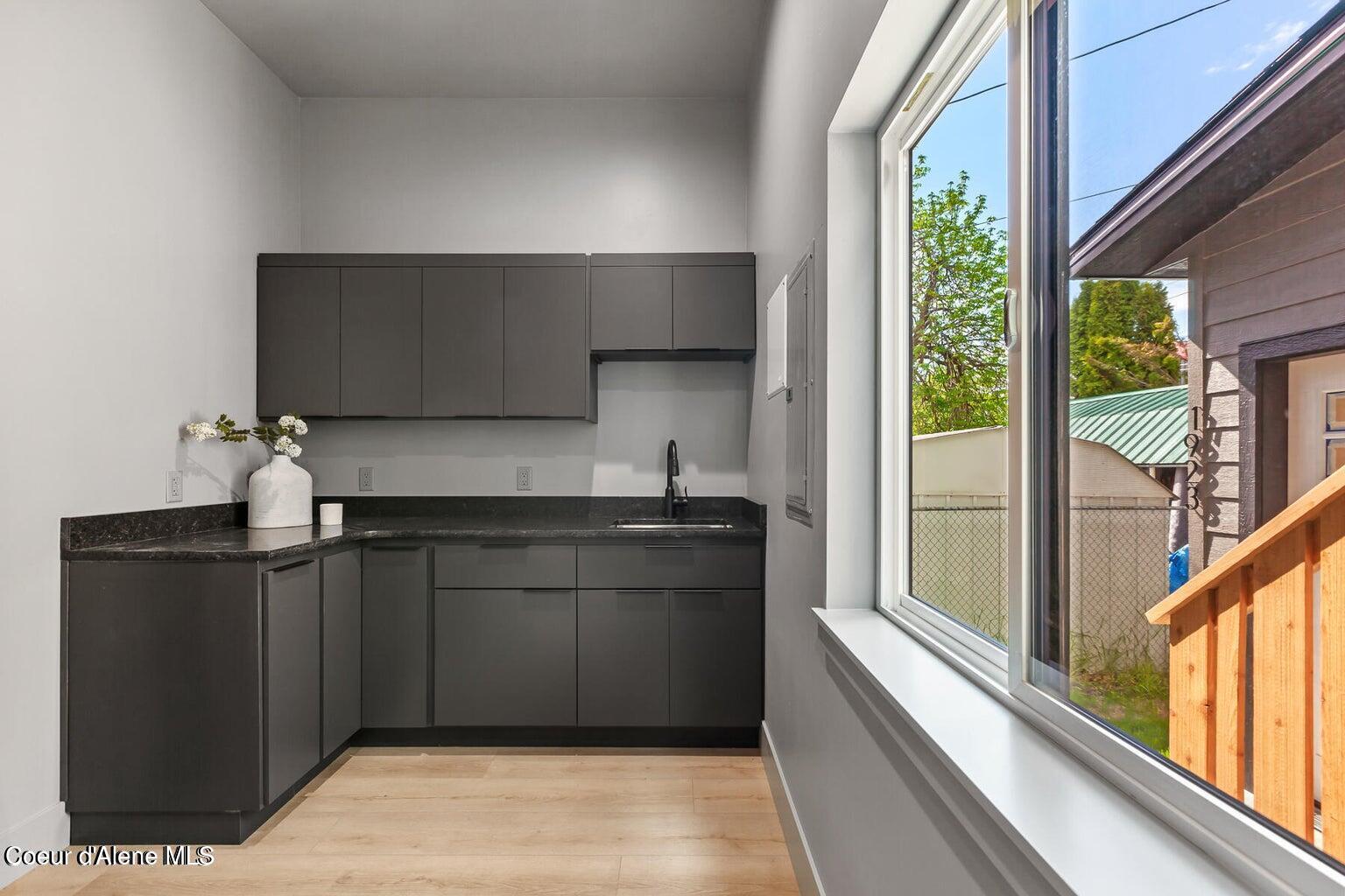 Compact kitchen with dark cabinets, black countertops, a small sink, and a large window.