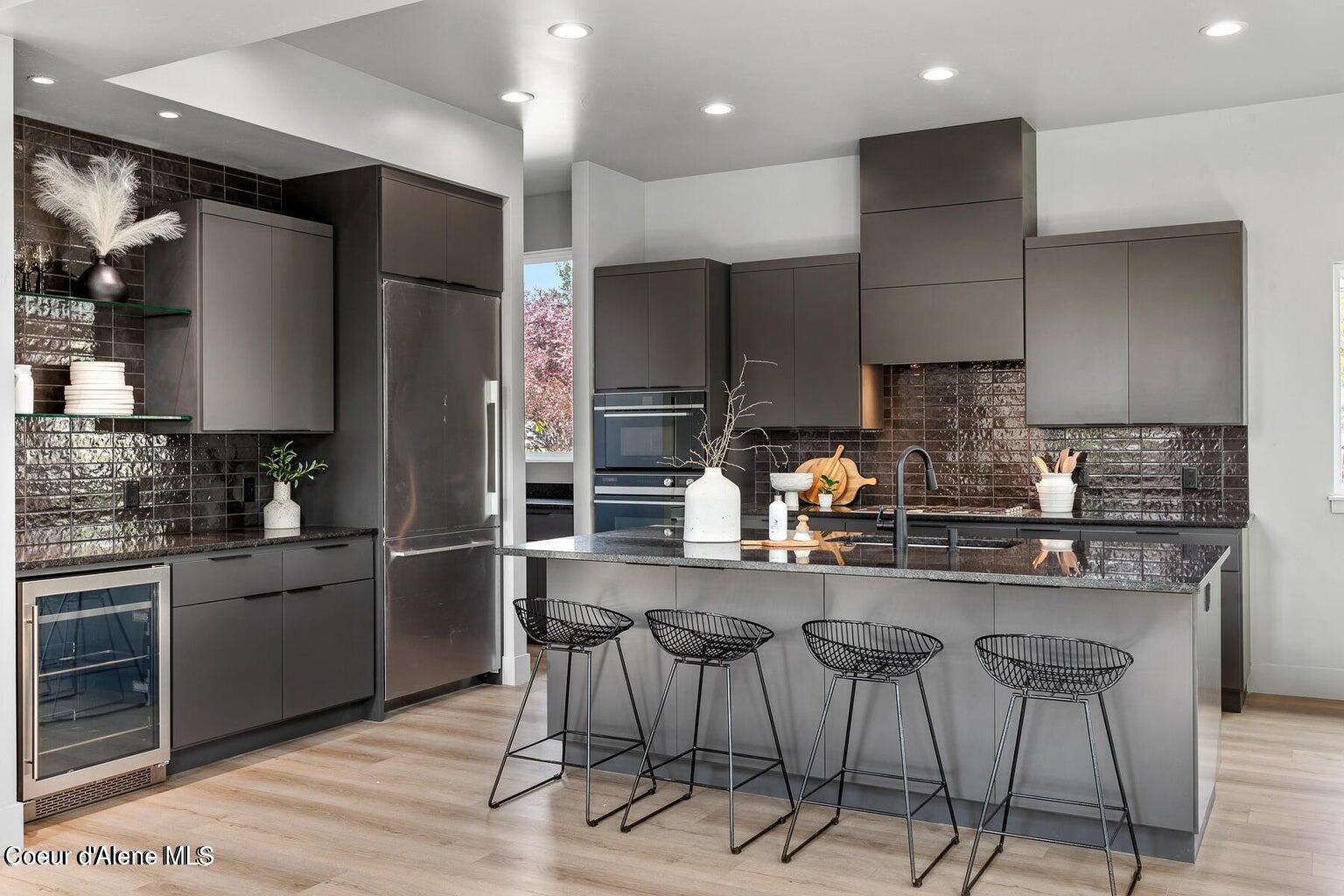 Modern kitchen with dark cabinetry, glossy tile backsplash, and a large island with four stools.