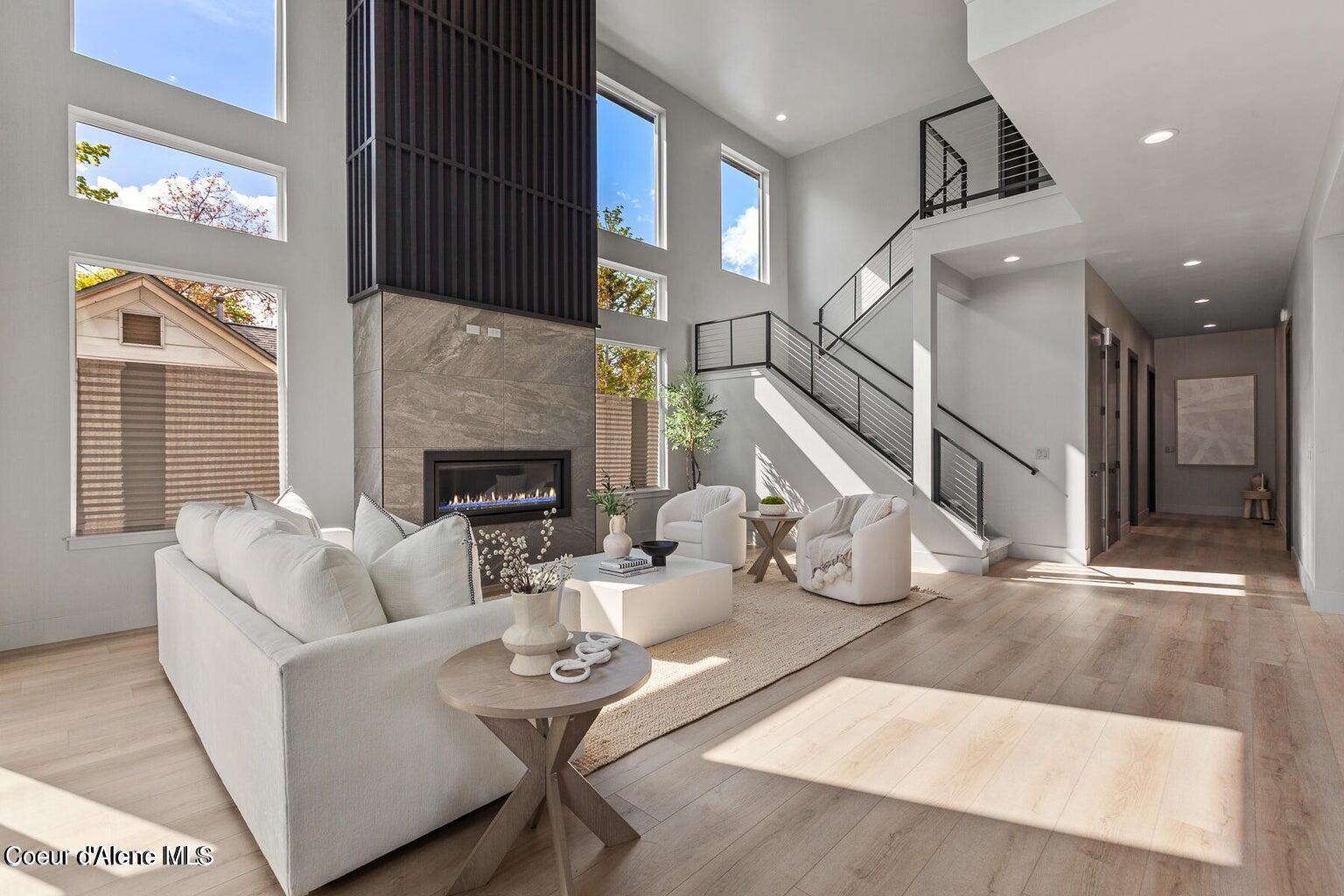 Double-height living room with a tall fireplace, large windows, white seating, and an open staircase.