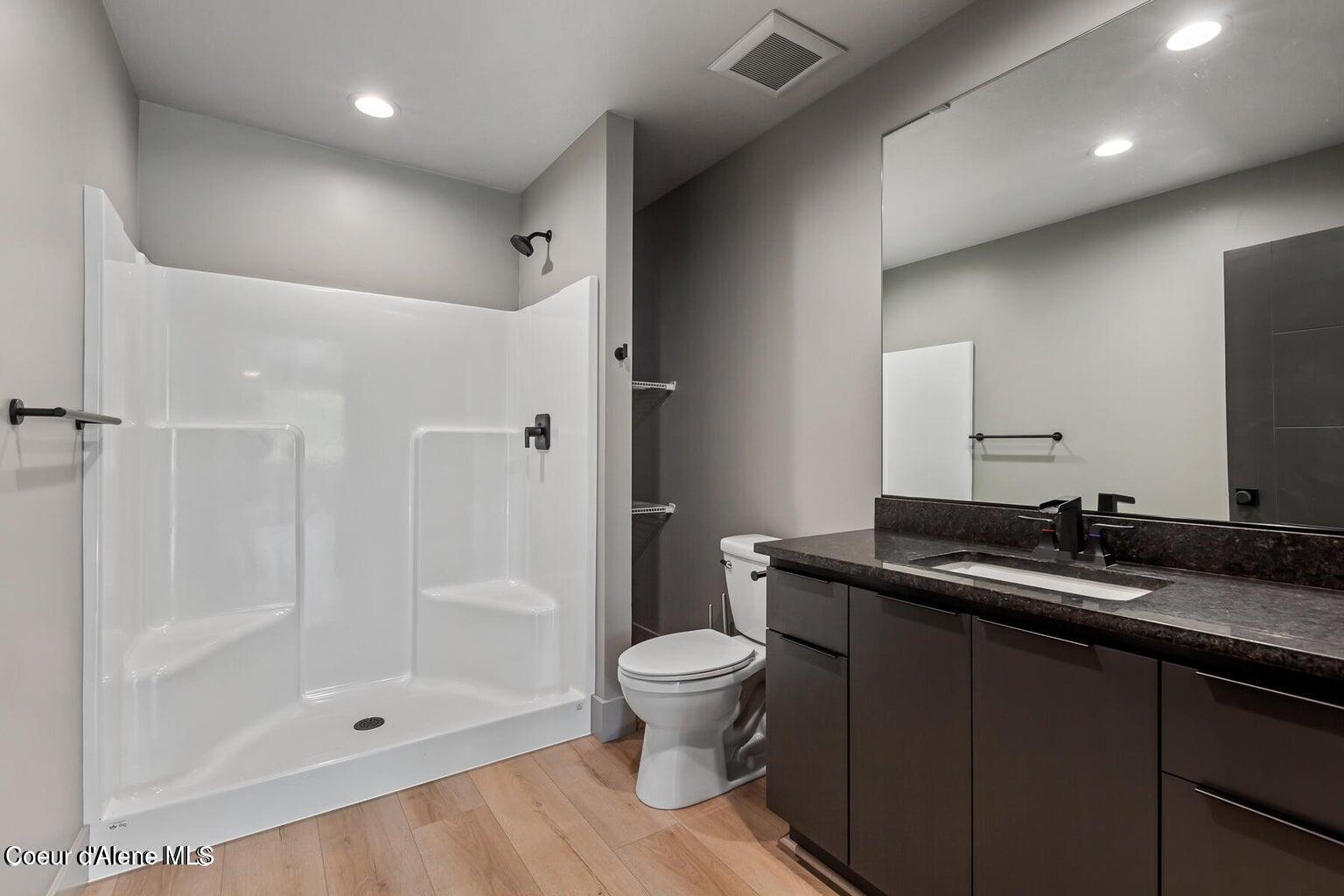 Bathroom with a white walk-in shower, dark vanity, and large wall mirror.