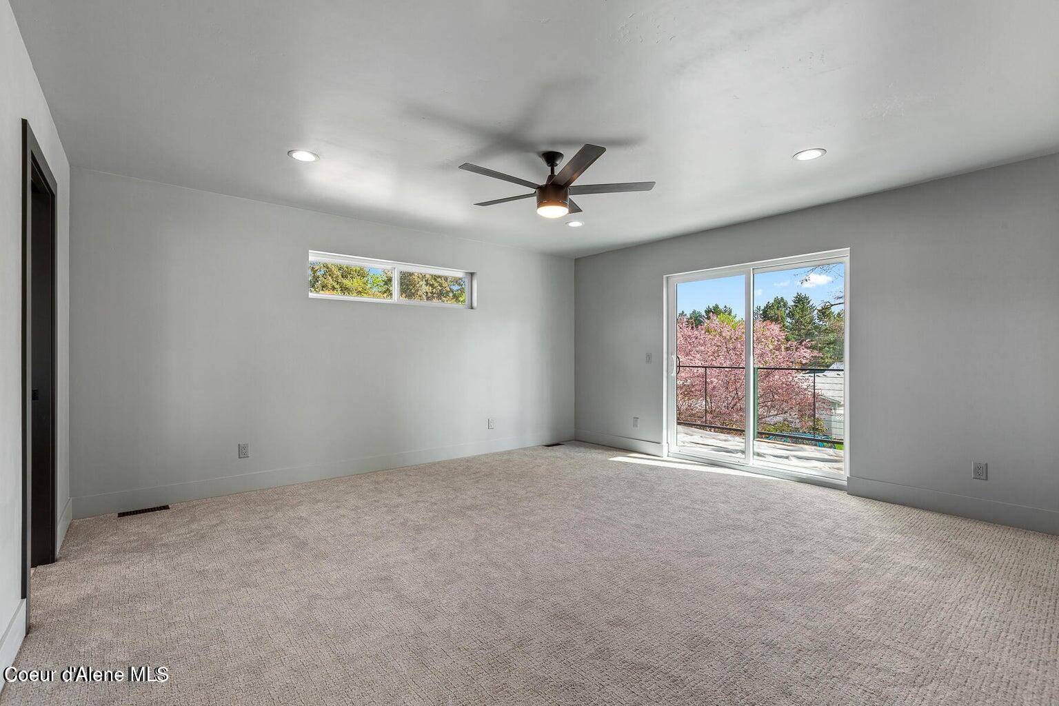 Empty carpeted bedroom with a ceiling fan and sliding glass doors opening to a balcony.