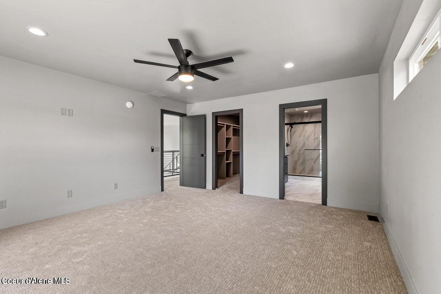 Unfurnished carpeted bedroom with a black ceiling fan and doors to a closet and tiled shower bathroom.