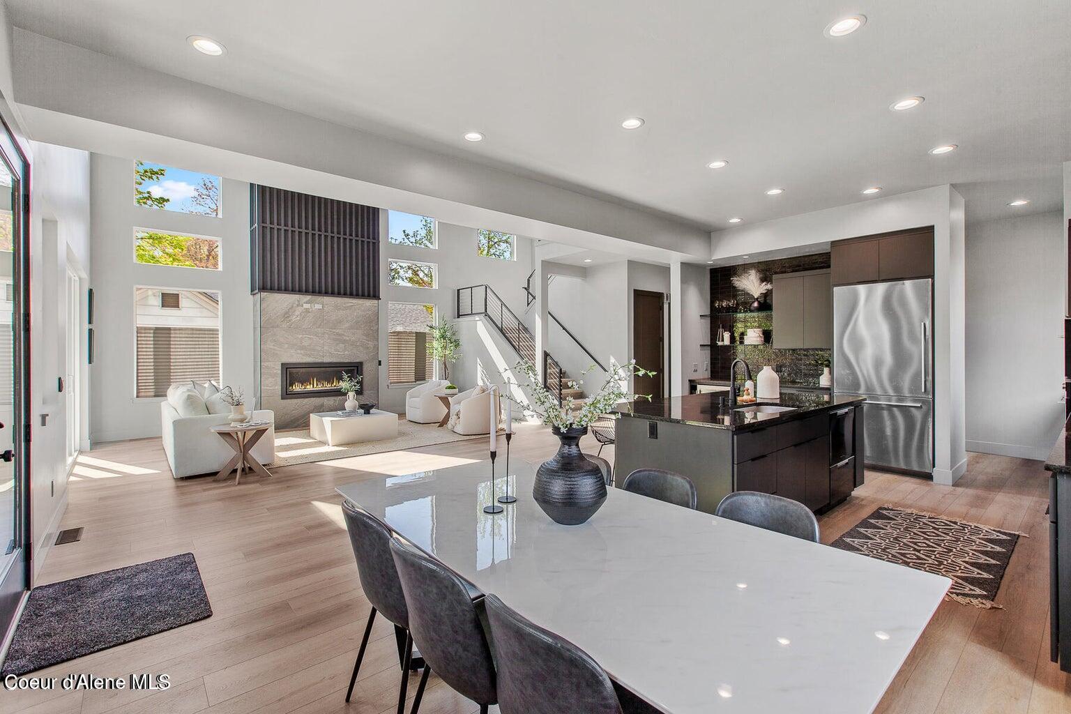 Open-plan living room and kitchen with a stone fireplace, tall windows, and a large dining table.