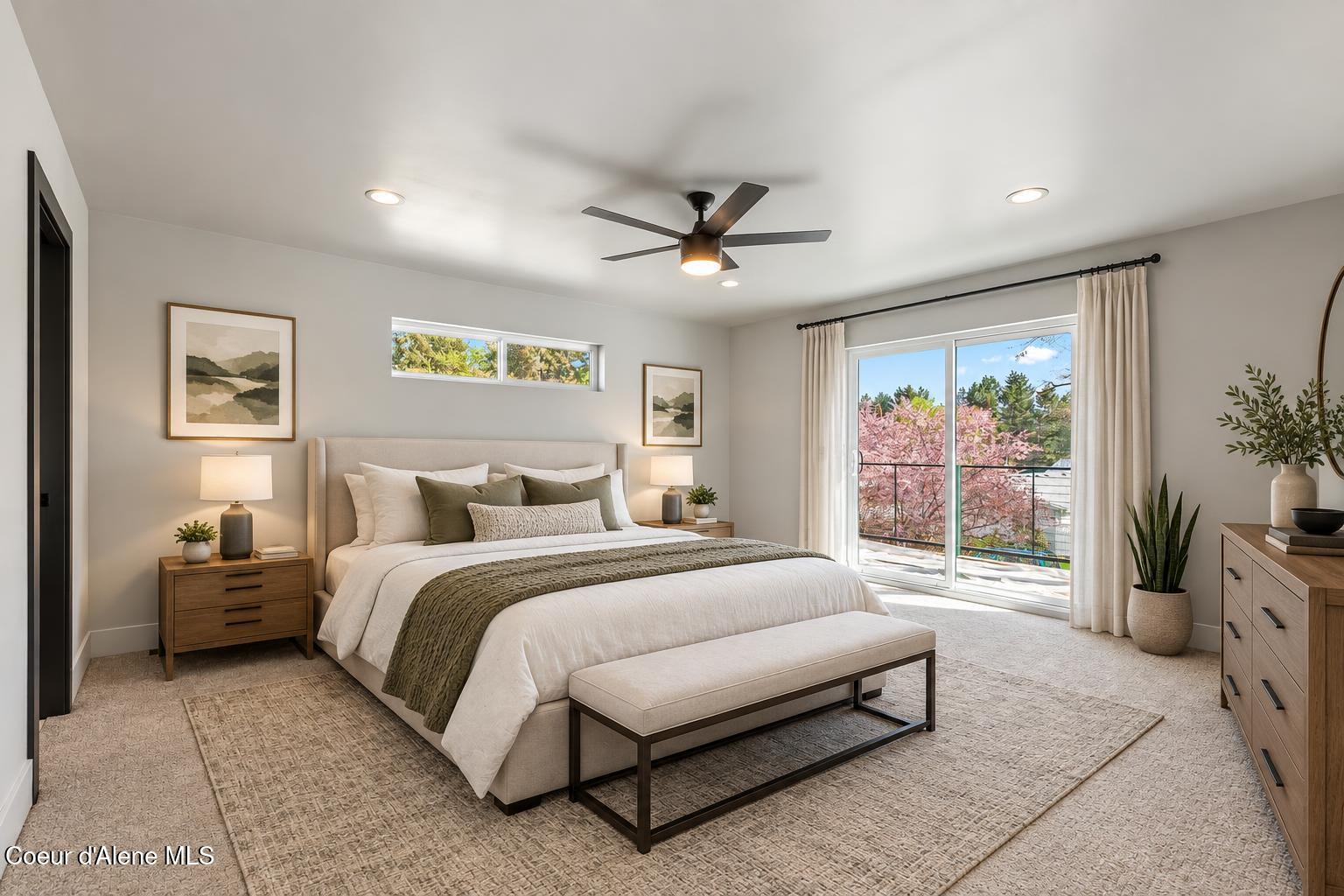 Staged bedroom with a king-size bed and sliding glass doors overlooking flowering trees.