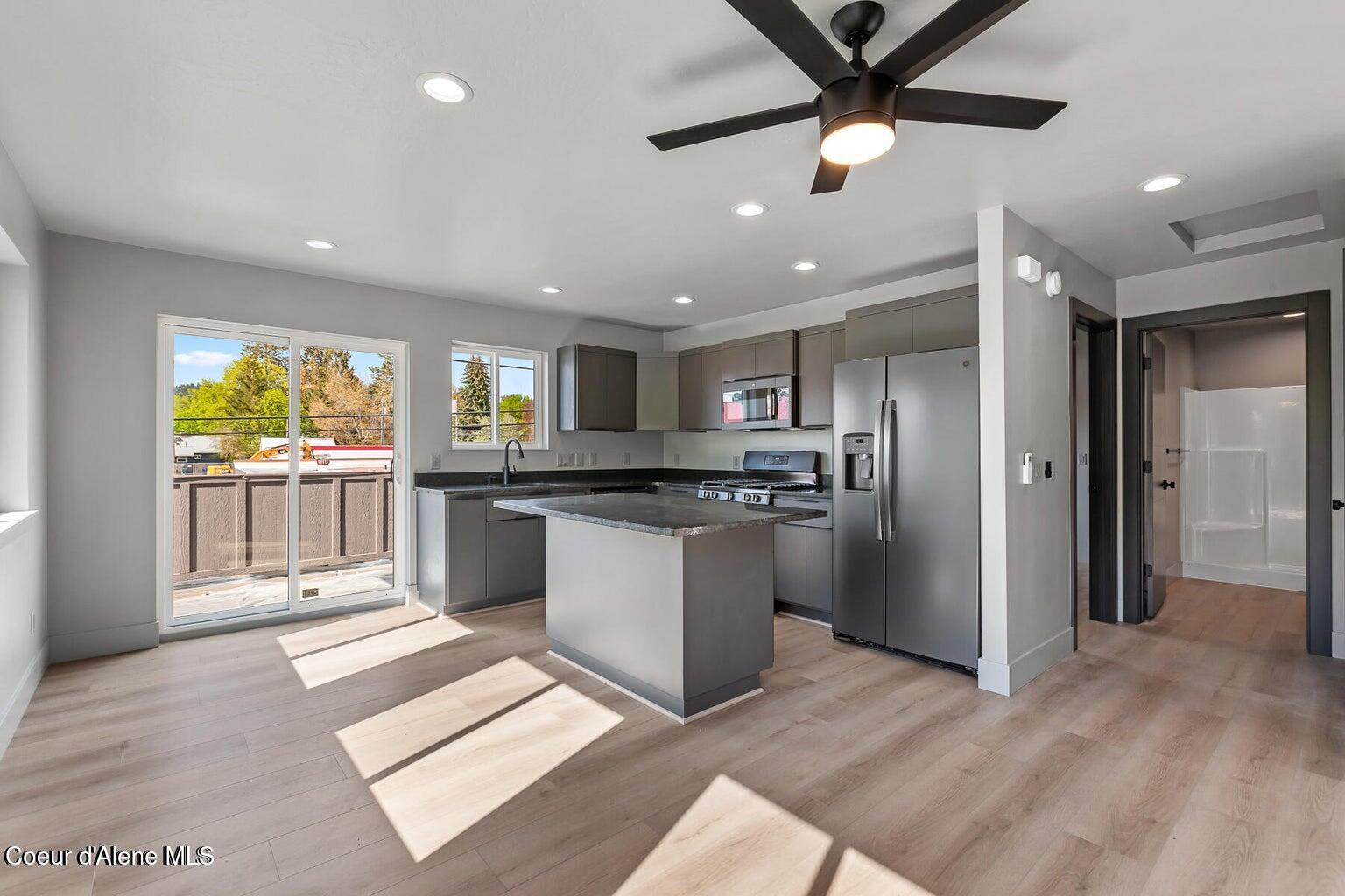 Modern kitchen with gray cabinets, stainless steel appliances, and an island beside a sunlit sliding glass door.
