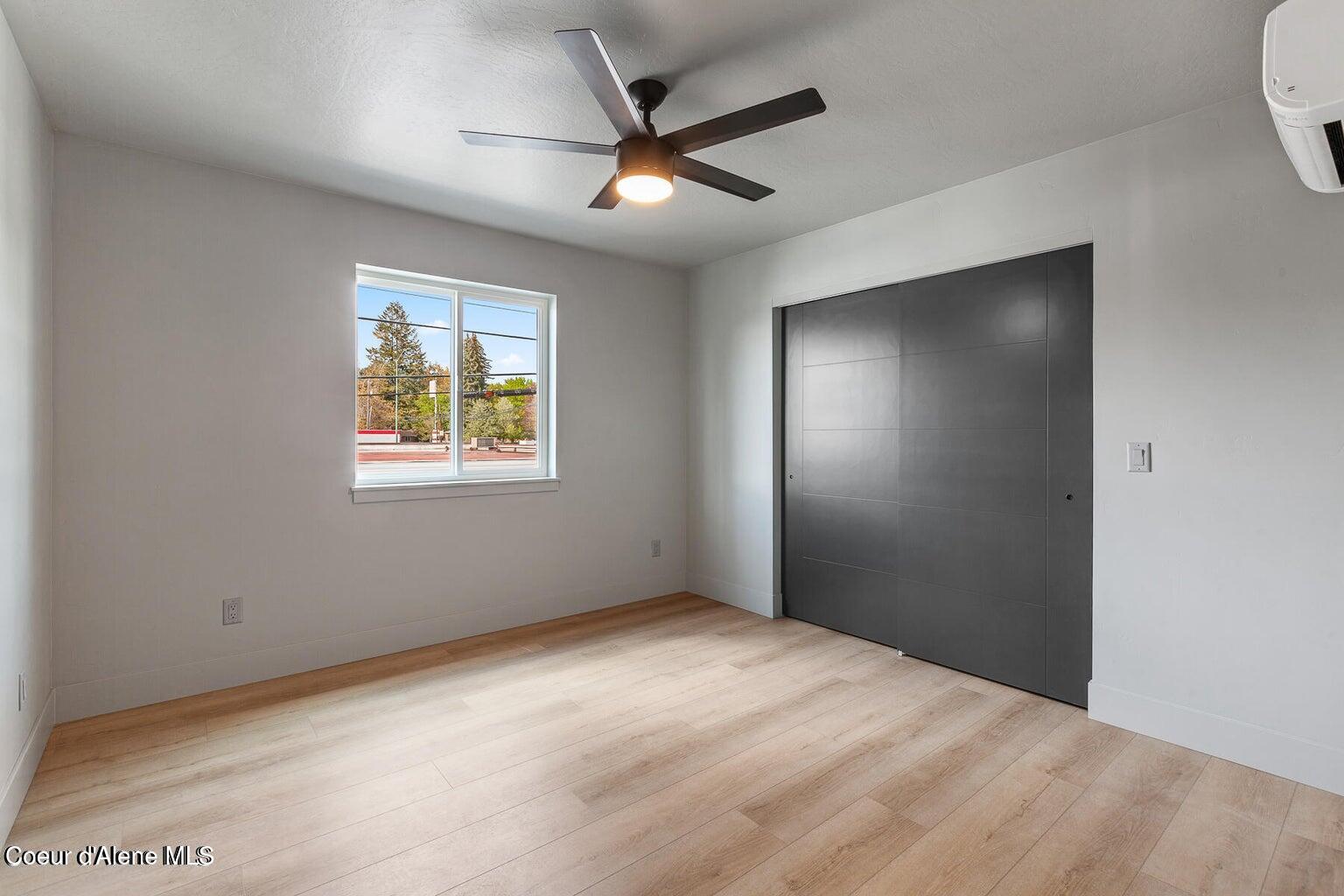 Empty room with light wood floors, dark sliding closet doors, and a ceiling fan with light.