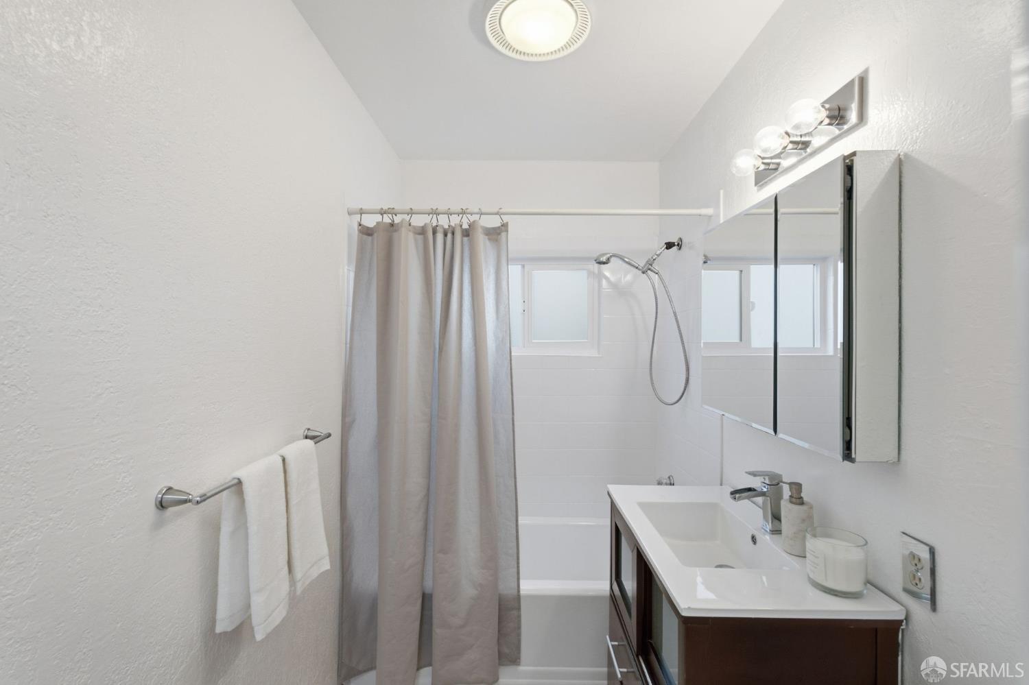 Bathroom with a bathtub, gray shower curtain, and white vanity beneath a mirrored cabinet.
