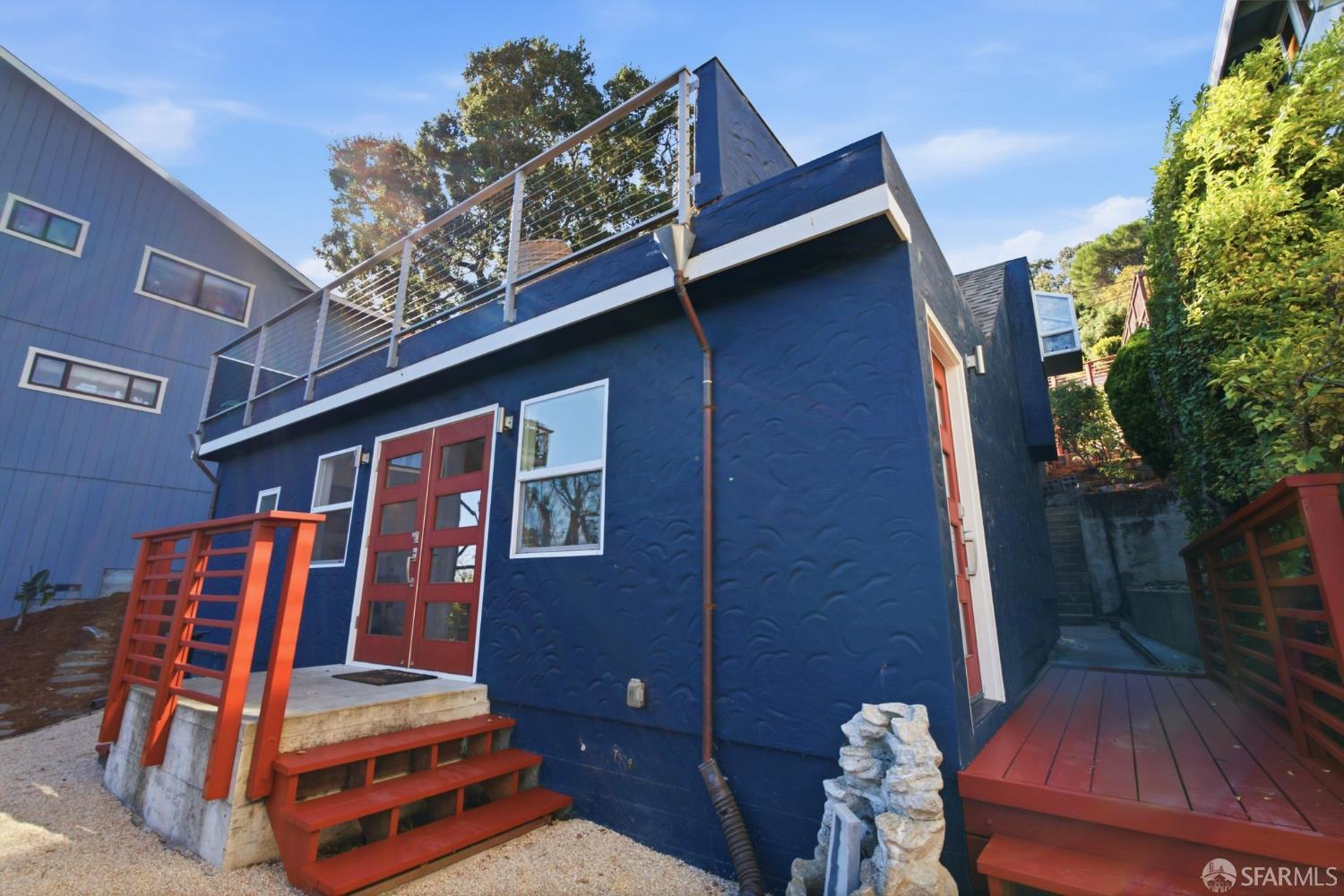 Dark blue house with red doors and stairs, a side deck, and an elevated rooftop terrace.
