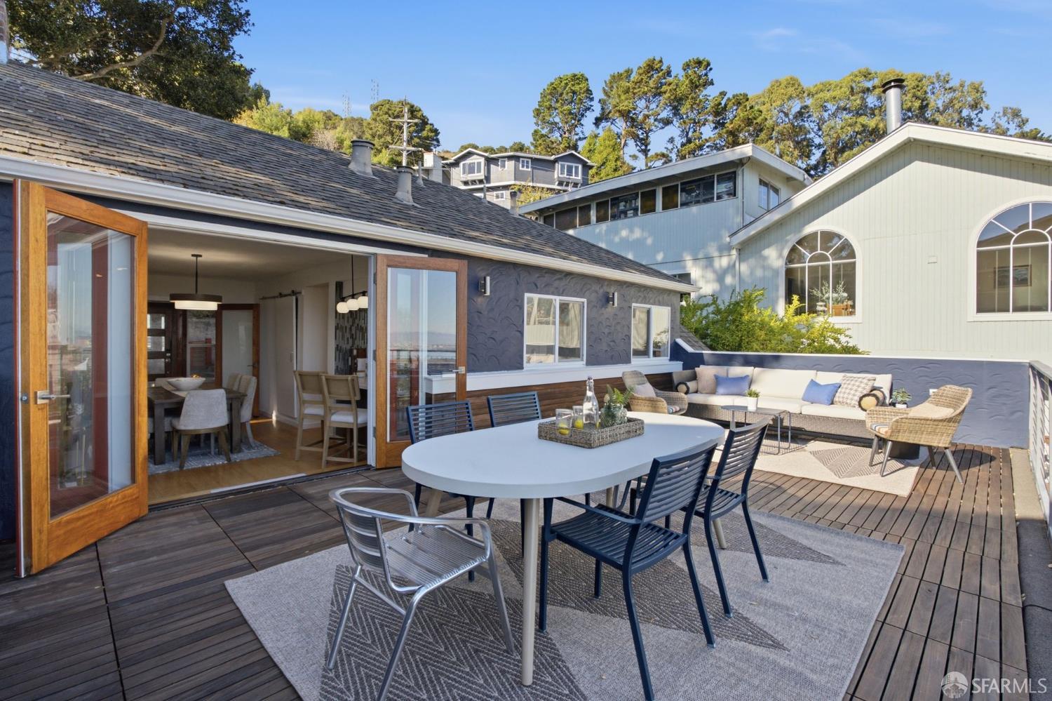 Outdoor deck with a dining table and lounge seating beside open folding doors.