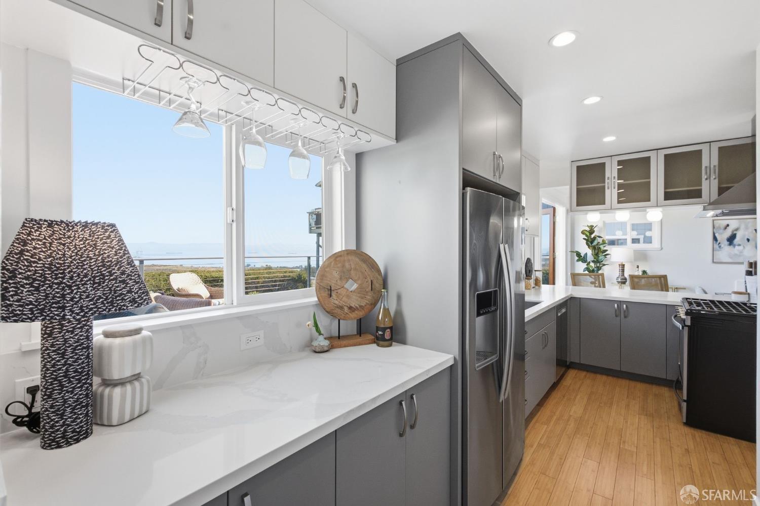 Modern kitchen with gray cabinets, white counters, and a large window overlooking the water.