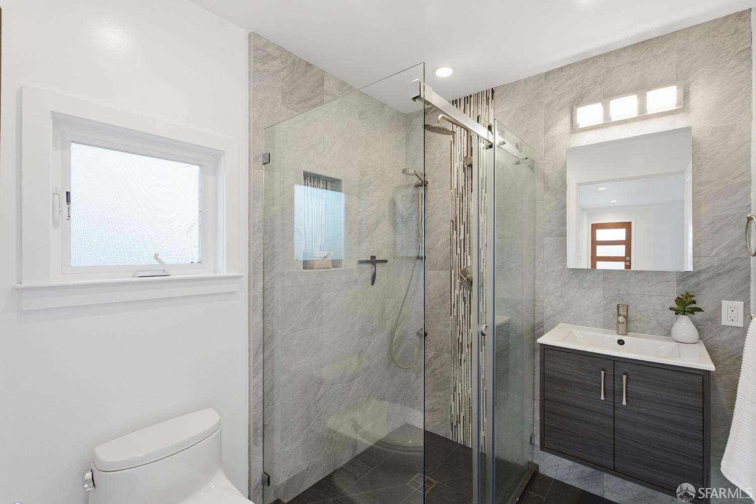 Remodeled bathroom with a glass walk-in shower, gray tile, and dark vanity.