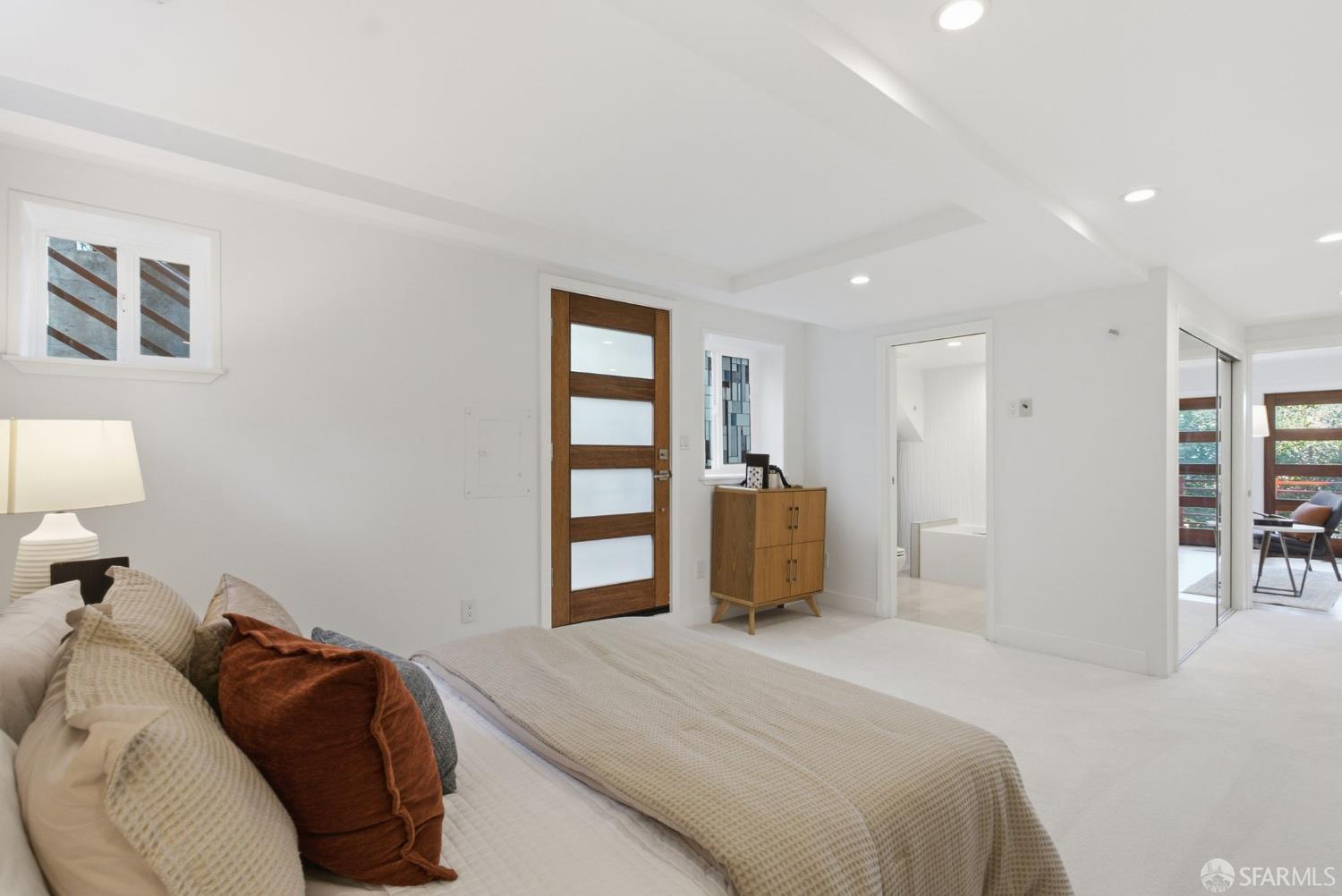 Furnished bedroom with a neutral bed, a wood-and-glass door, and a small wooden dresser.