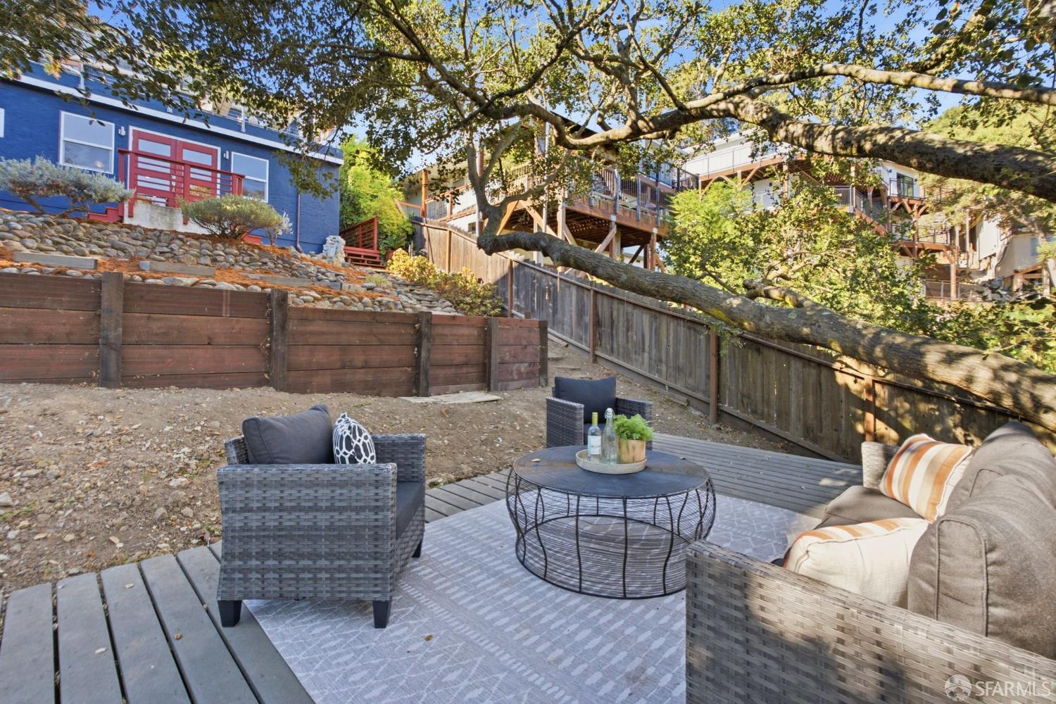 Outdoor patio with wicker seating and a round coffee table beneath a large tree.