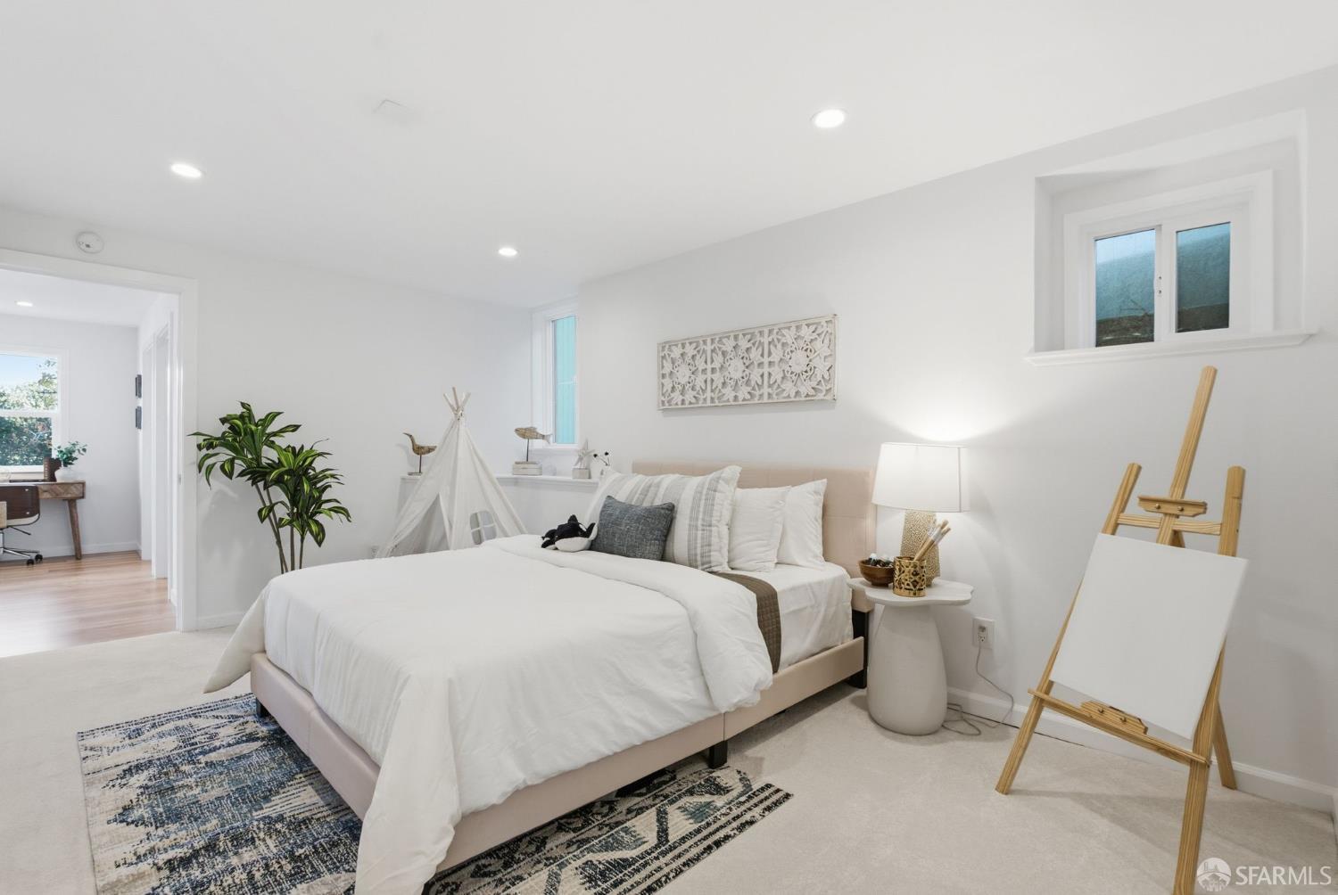 Staged bedroom with a white bed, patterned rugs, and an easel.