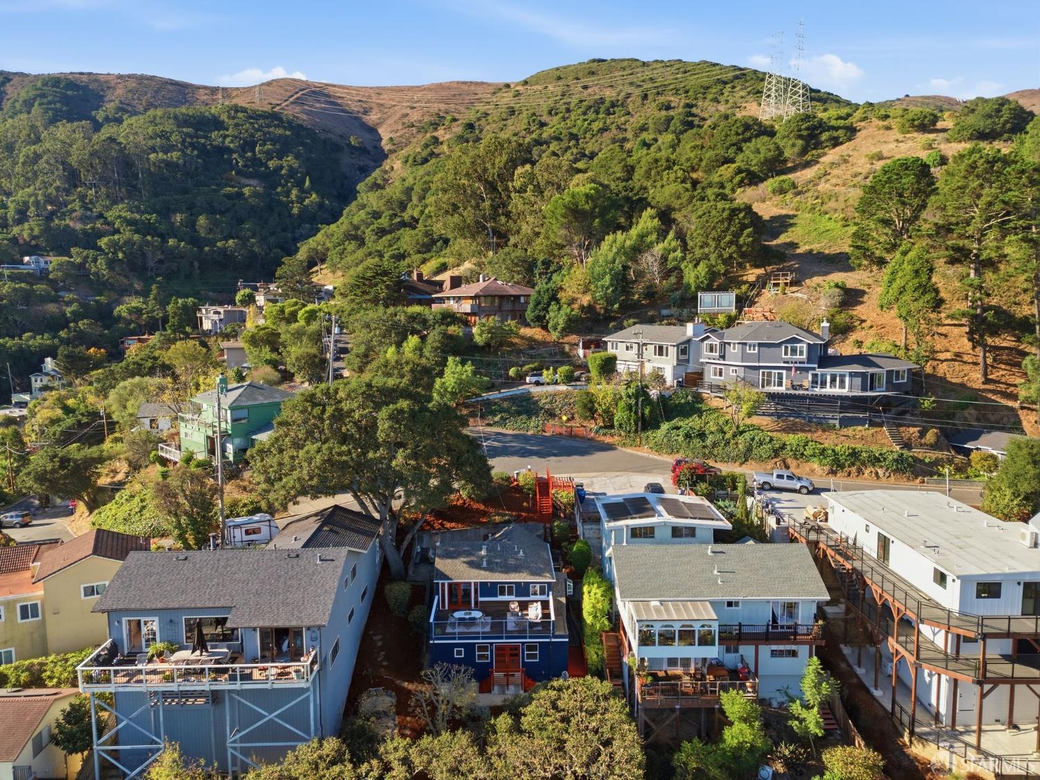 Aerial view of hillside homes below wooded slopes and a power transmission tower.