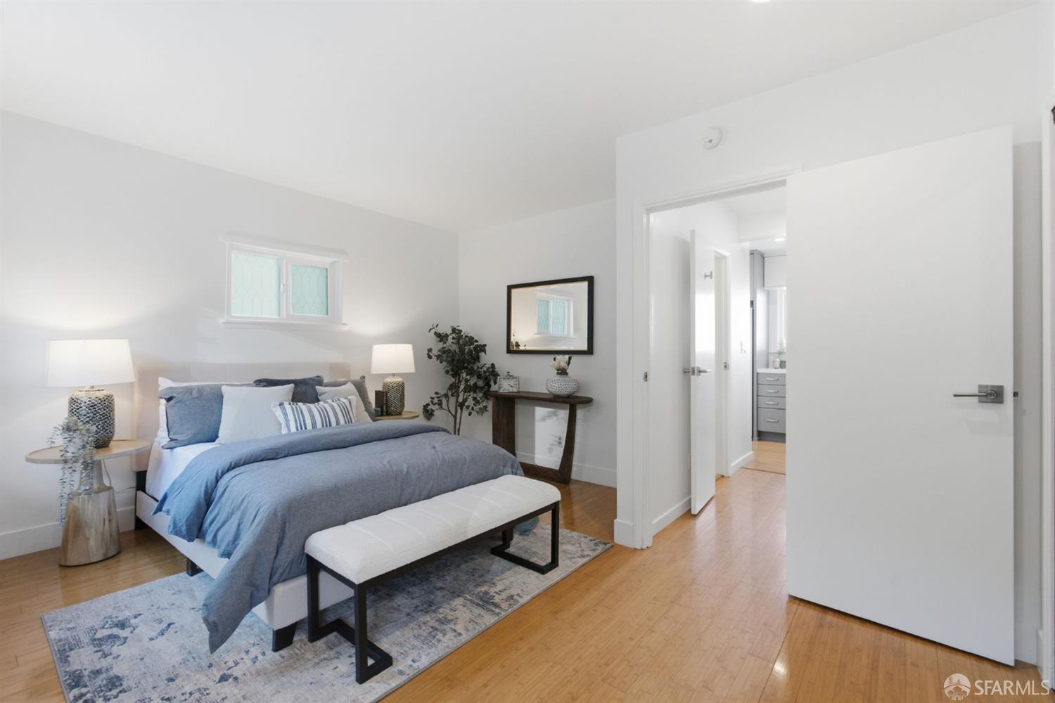 Staged bedroom with a blue-and-white bed, upholstered bench, and open doorway to the bathroom.