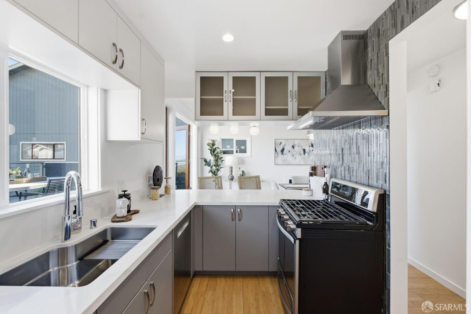 Remodeled kitchen with gray cabinets, white counters, a black range, and a stainless steel sink.