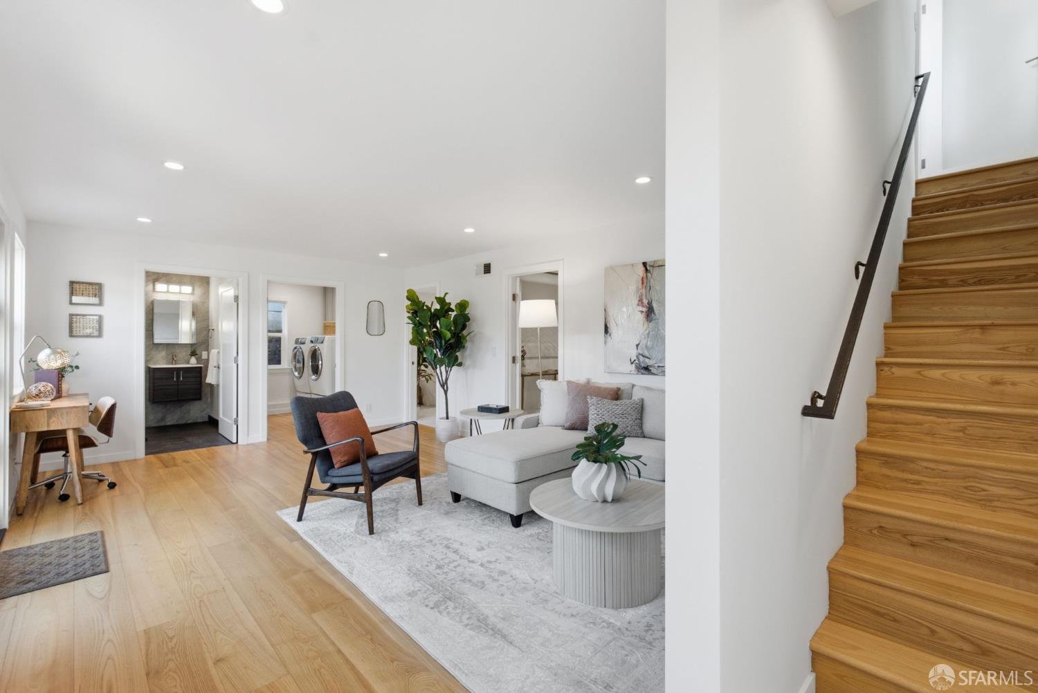 Bright living room with a white sectional and adjoining wooden staircase.