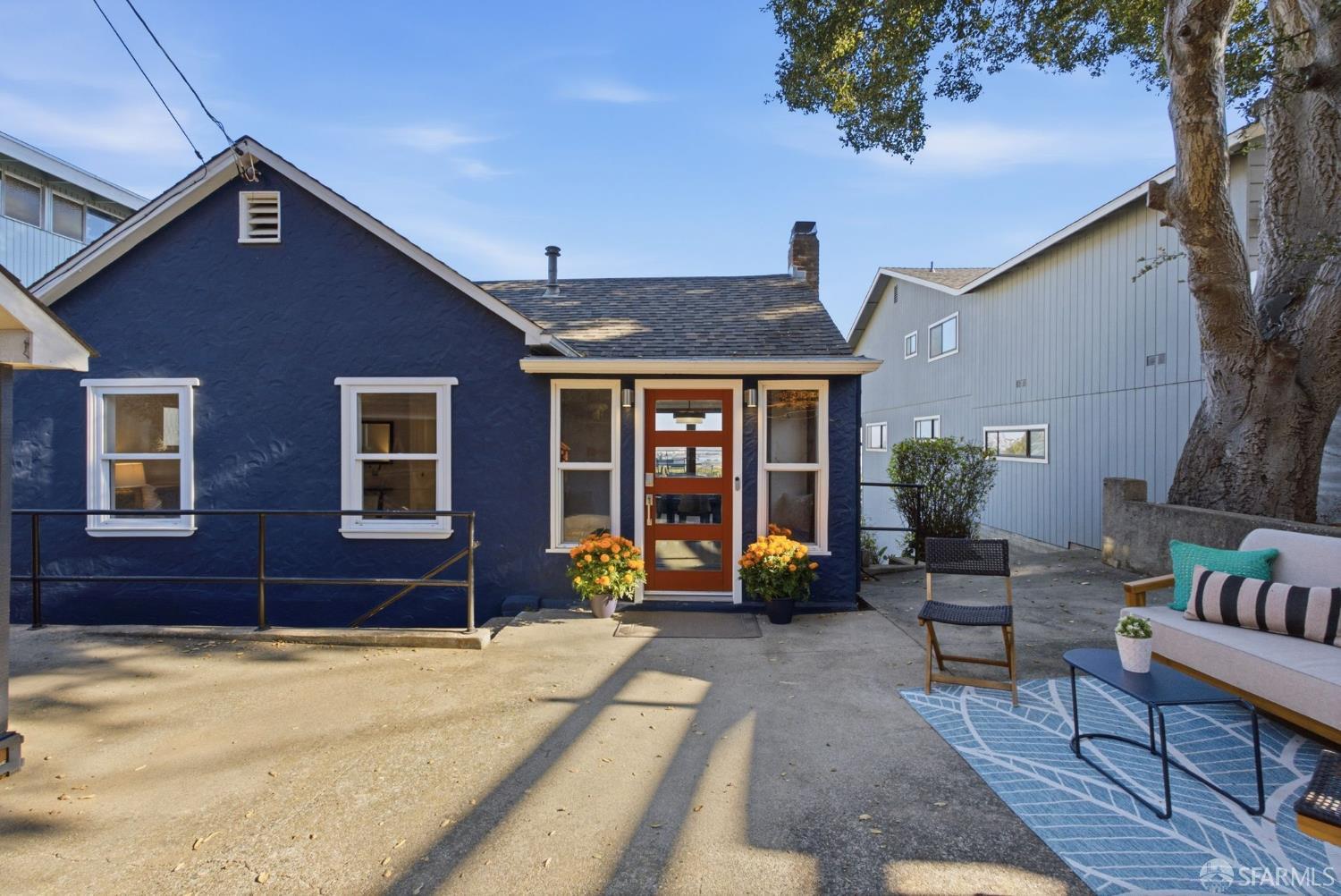 Navy-blue house with a red front door, potted flowers, and patio seating.
