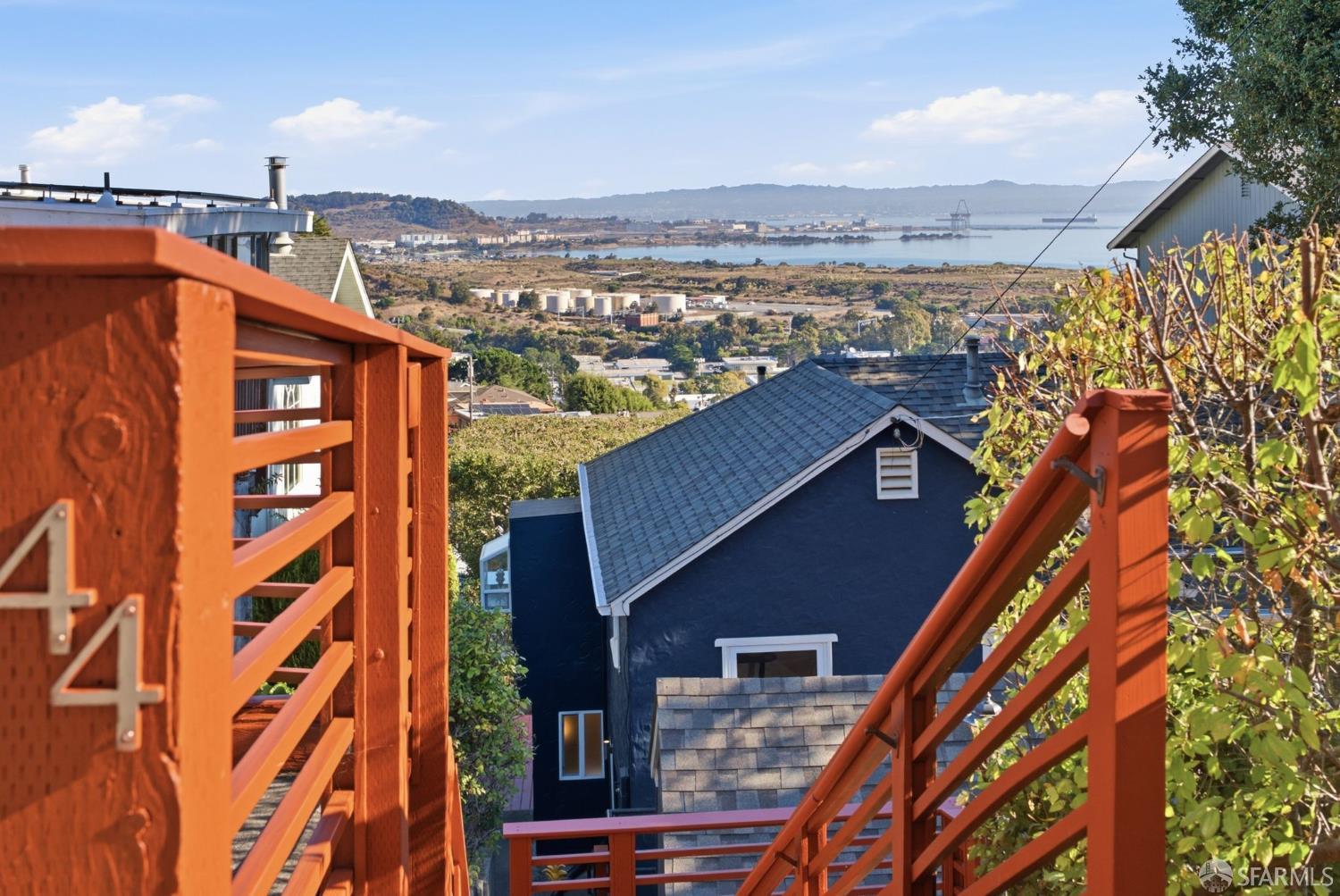 Bay view from orange-red wooden stairs overlooking nearby rooftops and distant hills.