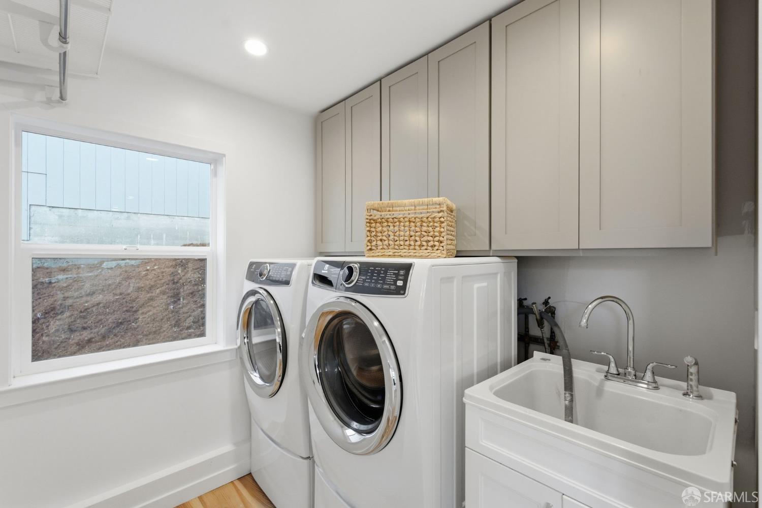 Laundry room with front-loading washer and dryer, gray cabinets, and a deep utility sink.